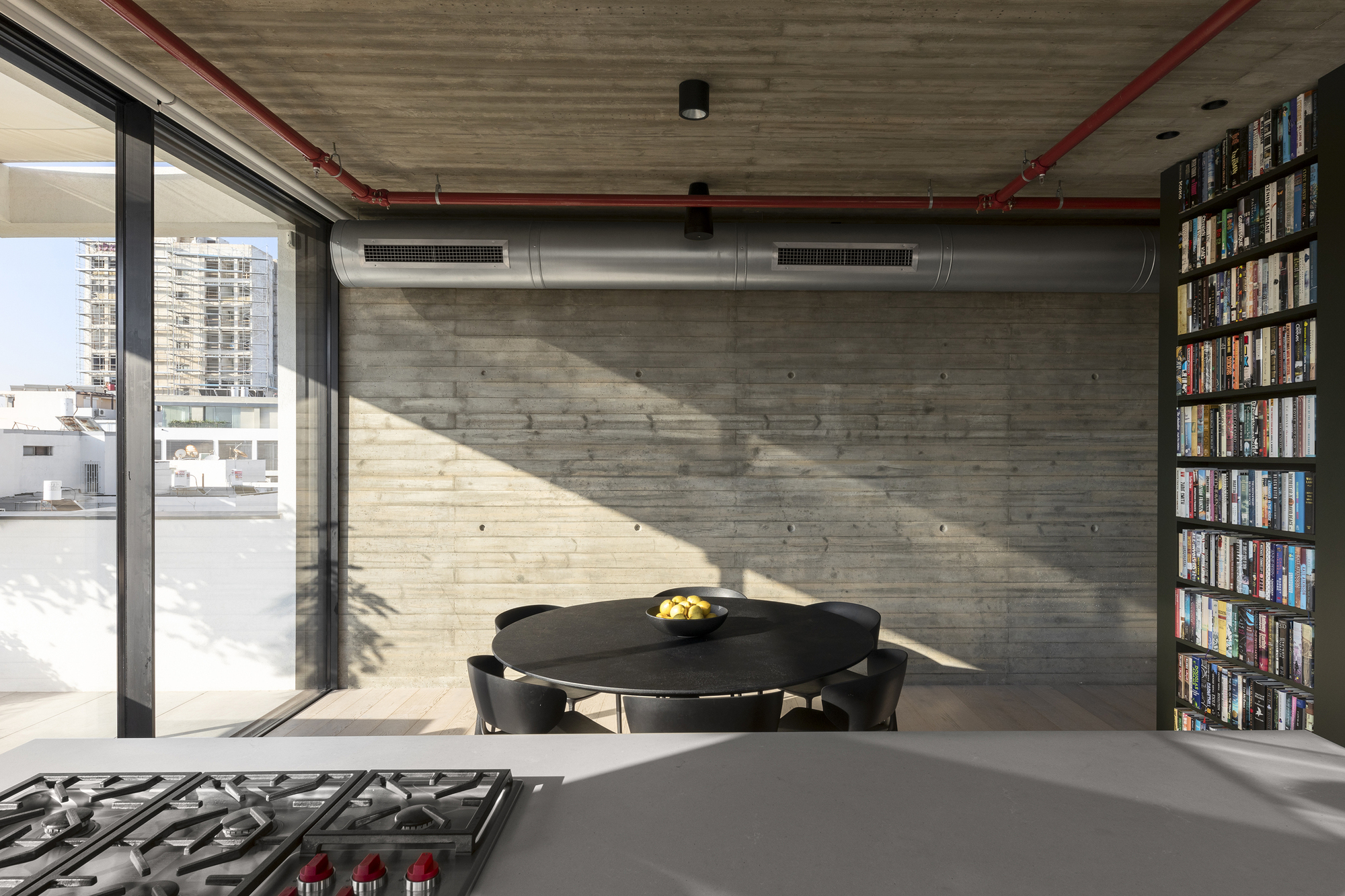 Dining area with exposed ductwork and red piping under board-formed concrete ceiling with bright sunlight streaming in