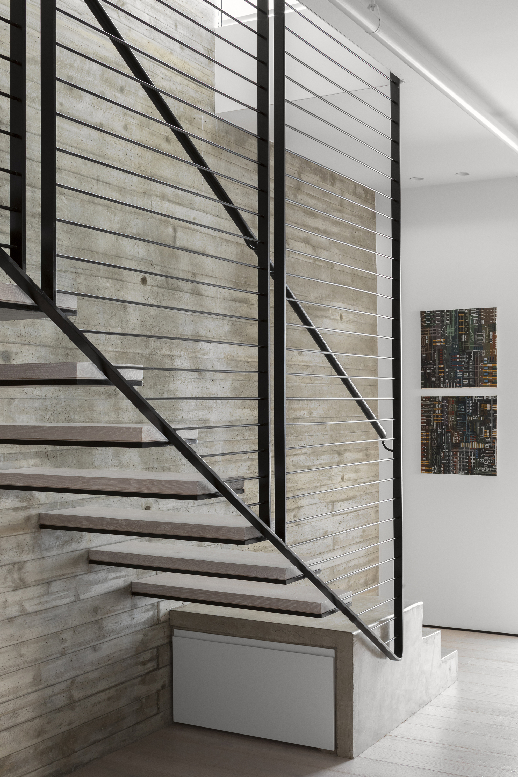 Steel floating staircase with horizontal cable railing against board-formed concrete wall under a skylight