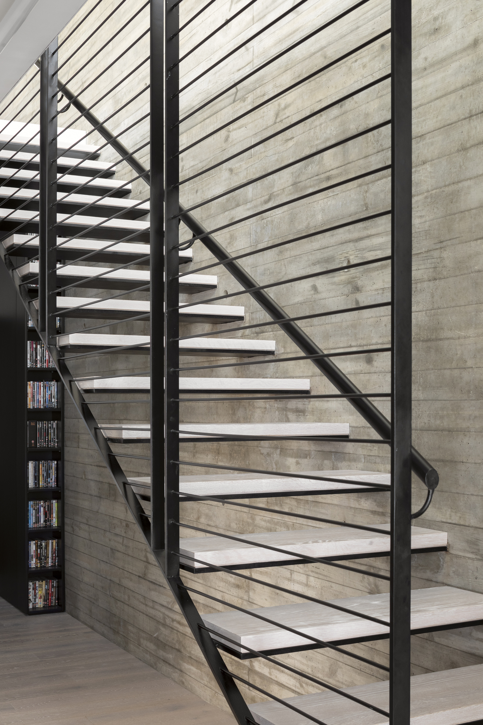 Close-up of cantilevered steel stair treads with horizontal cable railing against board-formed concrete wall