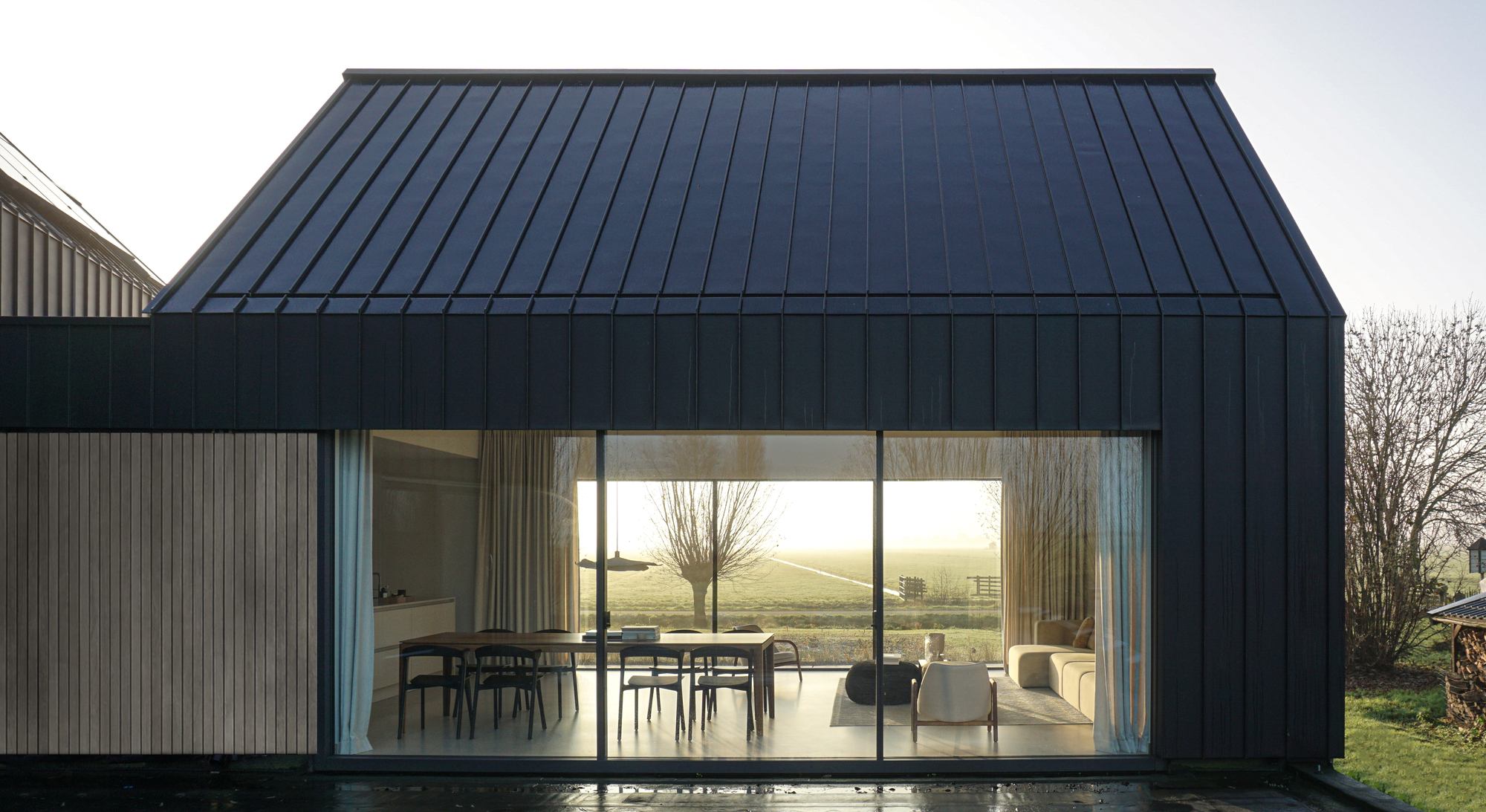 Full-height glazed wall opening onto a terrace with views of pollarded trees and distant fields