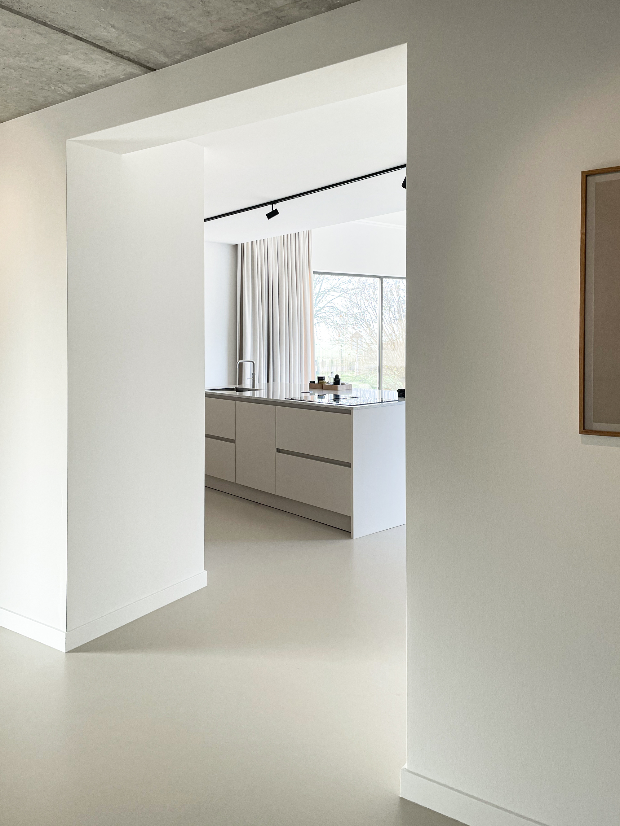 Threshold between rooms with exposed concrete ceiling and pale resin floor