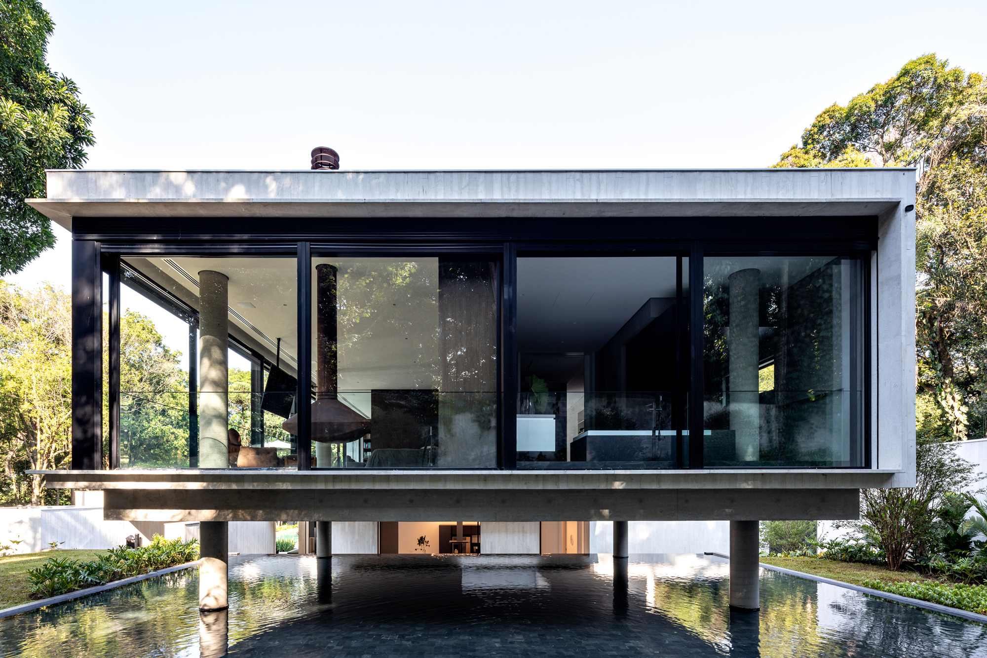 Elevated concrete volume with full-height glazing and dark frames above a reflecting pool