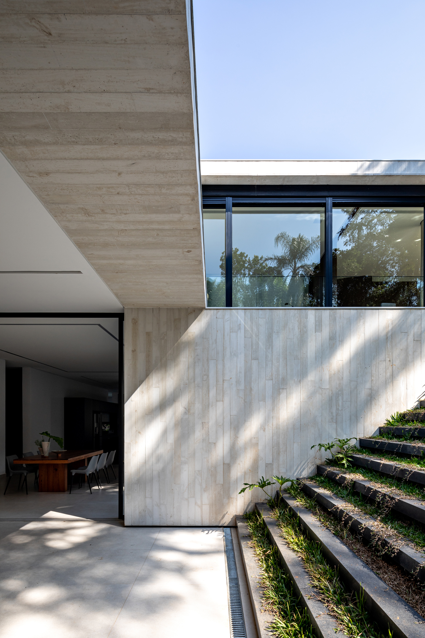 Board-formed concrete wall beside planted steps leading to the garden in dappled sunlight