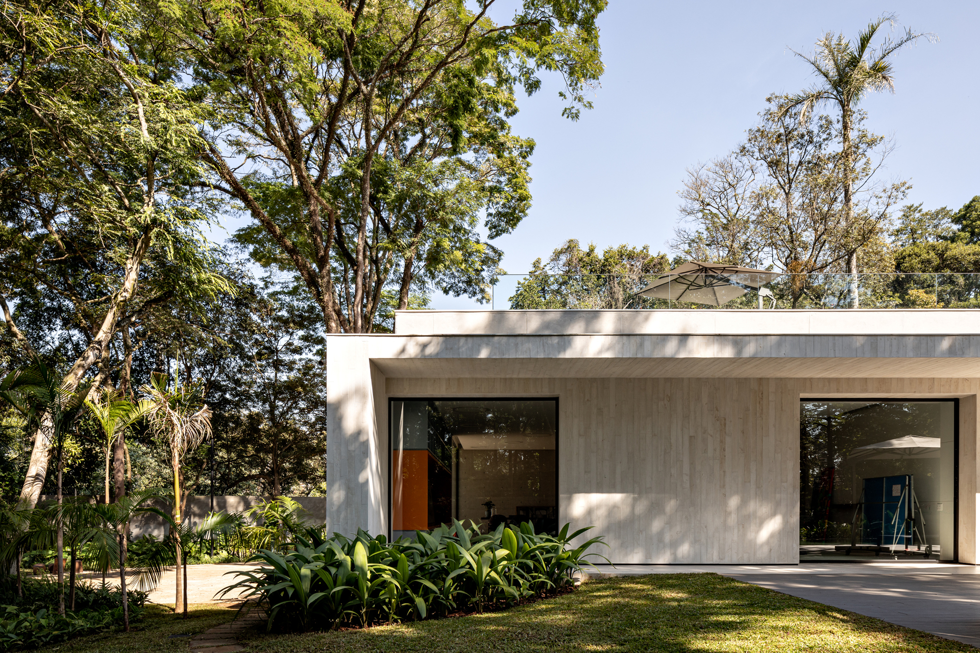 Single-story pavilion with board-formed concrete facade and large glazed openings set in lawn under mature trees