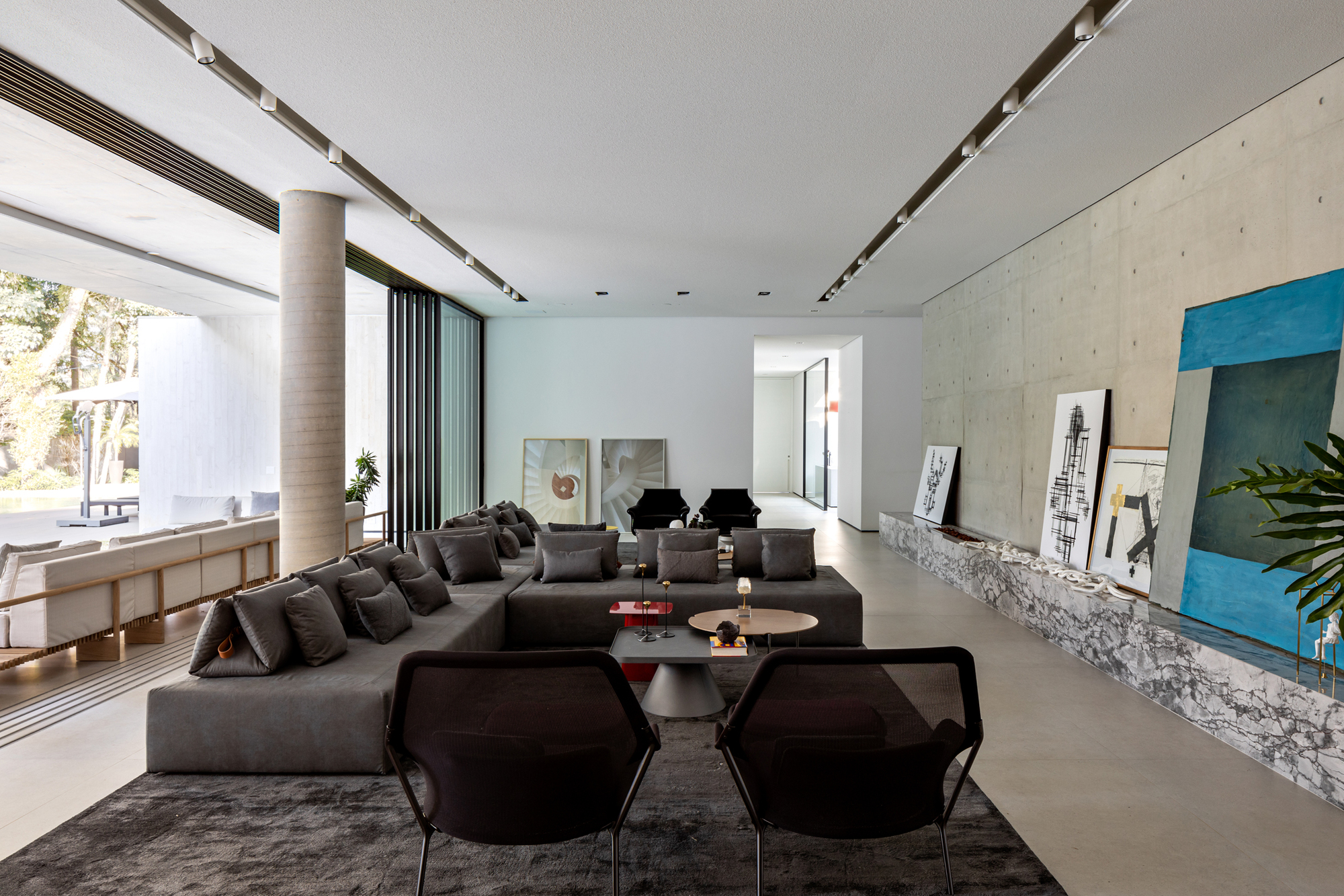This architectural image showcases a modern living room with a spacious open floor plan. The design features a large gray sectional sofa, a concrete accent wall