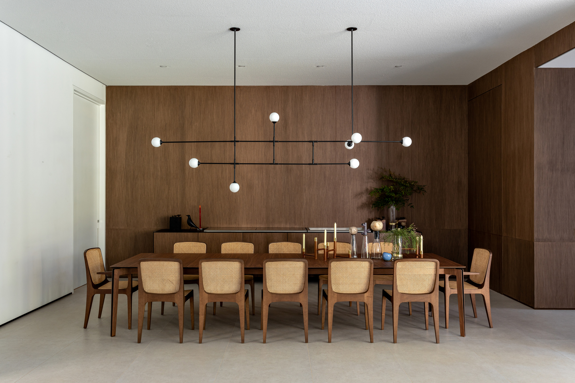 This architectural image showcases a modern dining room with a focus on natural materials and clean lines. The room features wood paneling, a large wooden dinin