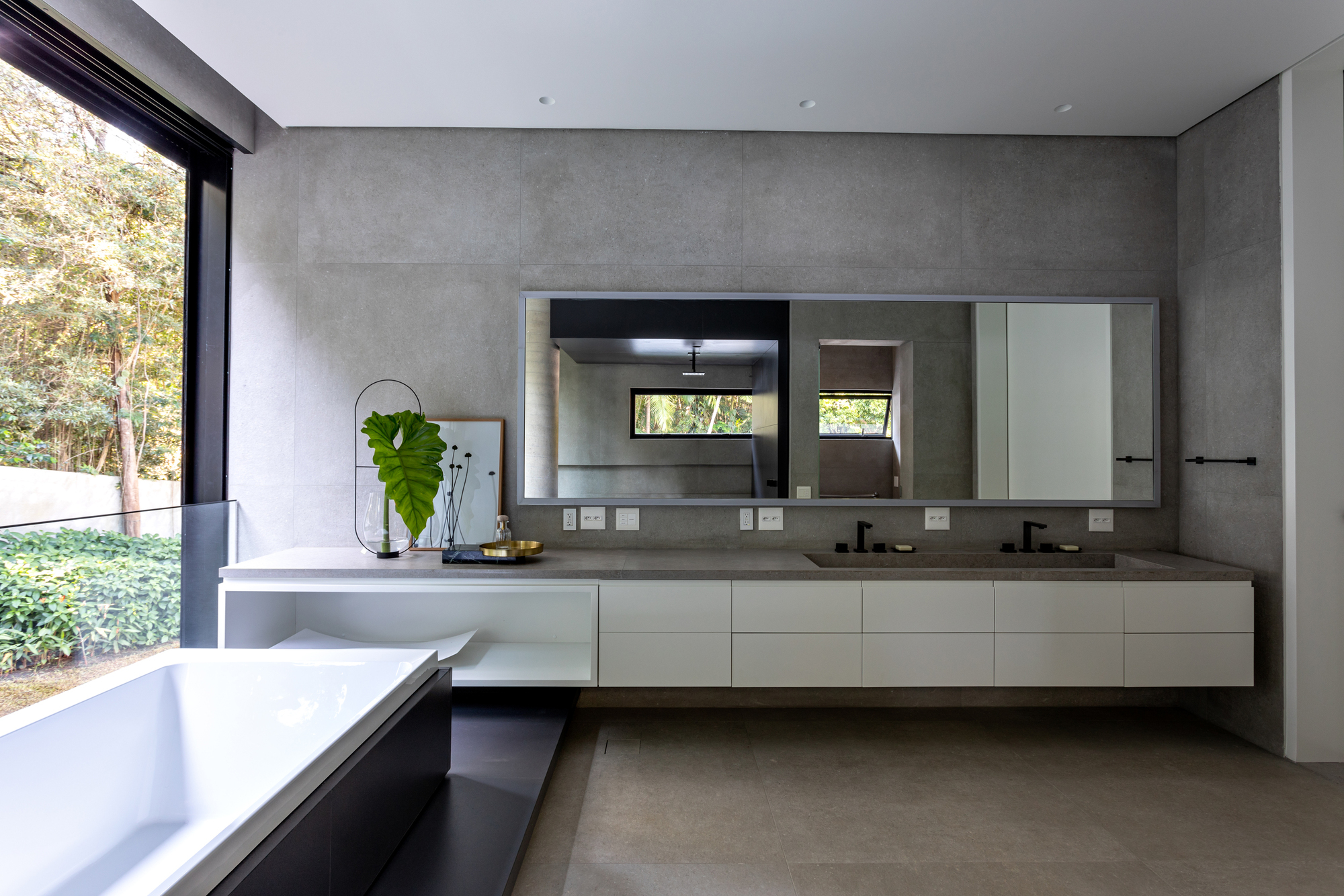 Bathroom with floating white vanity beneath concrete panel walls and a planted courtyard beyond