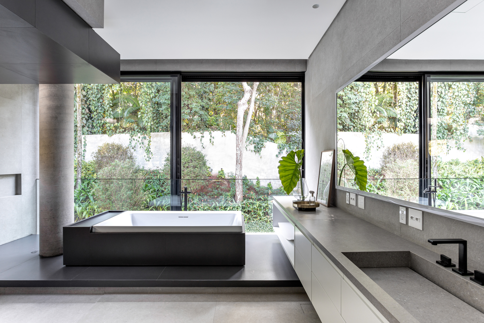 Freestanding bathtub on a black plinth framed by windows opening to a landscaped garden