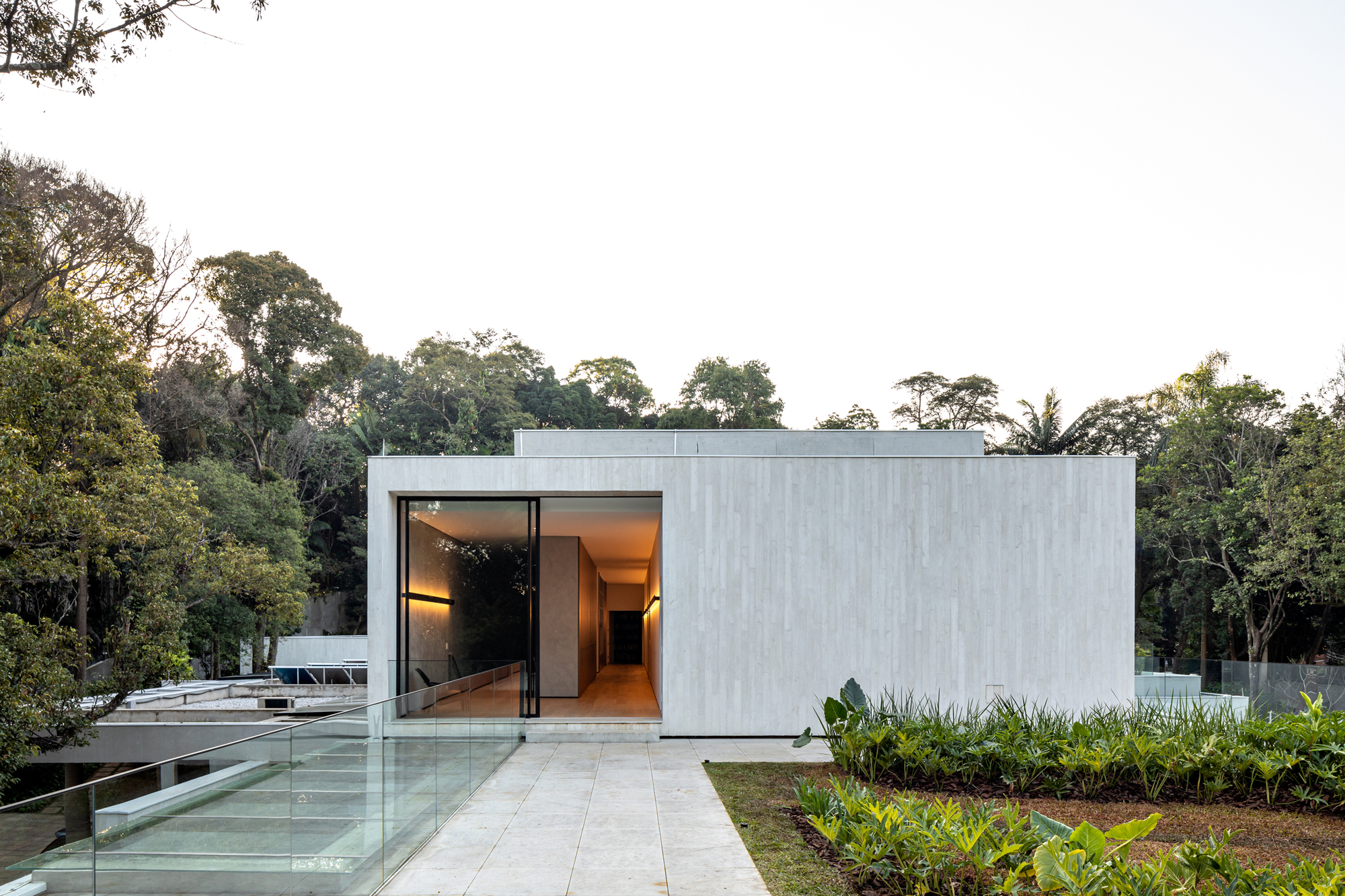 Rectilinear concrete volume with large glass opening approached by a stone-paved pathway flanked by planted beds