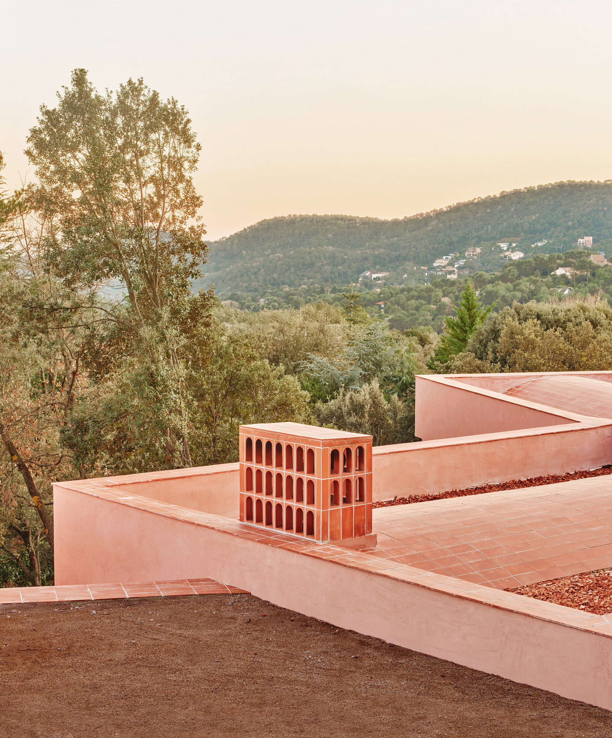 Terraced roof with terracotta chimney structure overlooking forested hillside at dusk