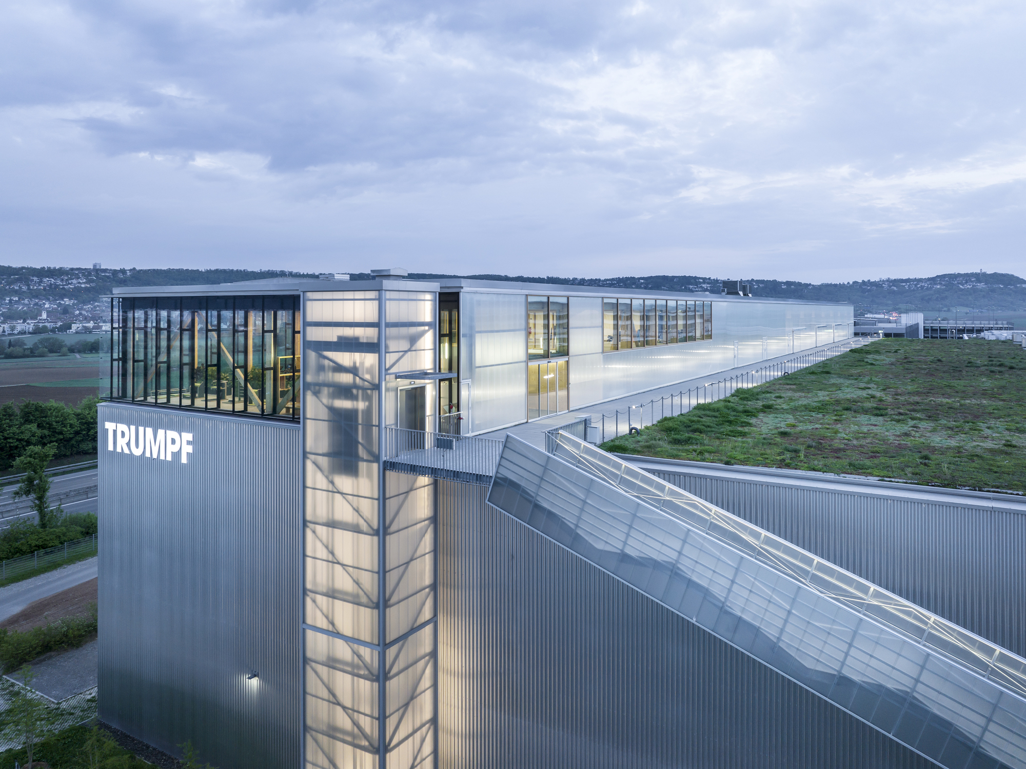Tower element with vertical glass stairwell and corrugated metal cladding at twilight