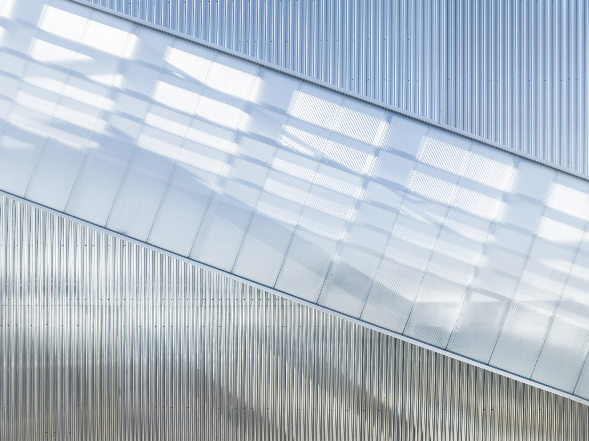 Close-up of the angled glazed bridge against vertically ribbed metal cladding