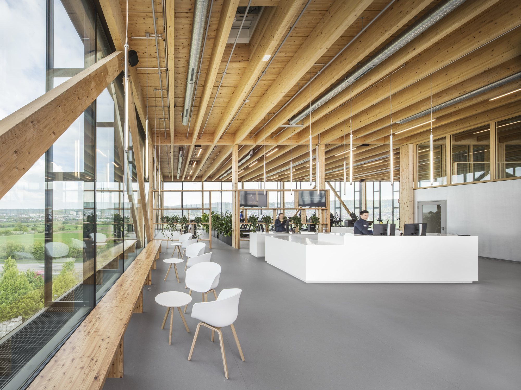 Open plan office space with exposed timber beam ceiling and full-height glazing overlooking green fields