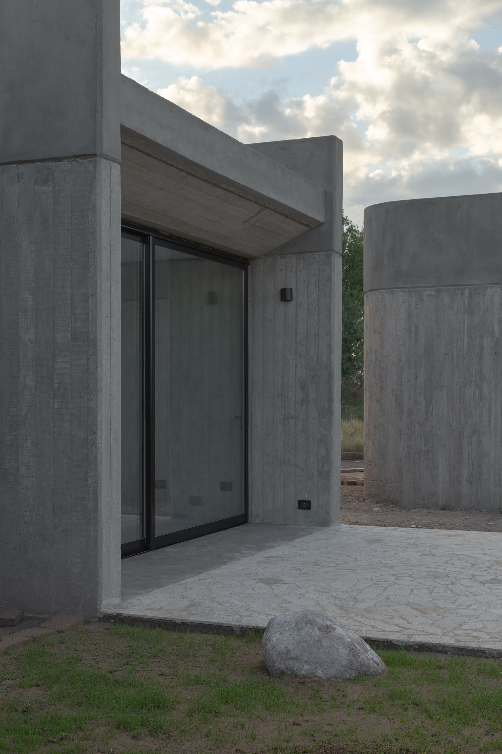 Recessed glass door beneath a concrete canopy flanked by cylindrical concrete volumes