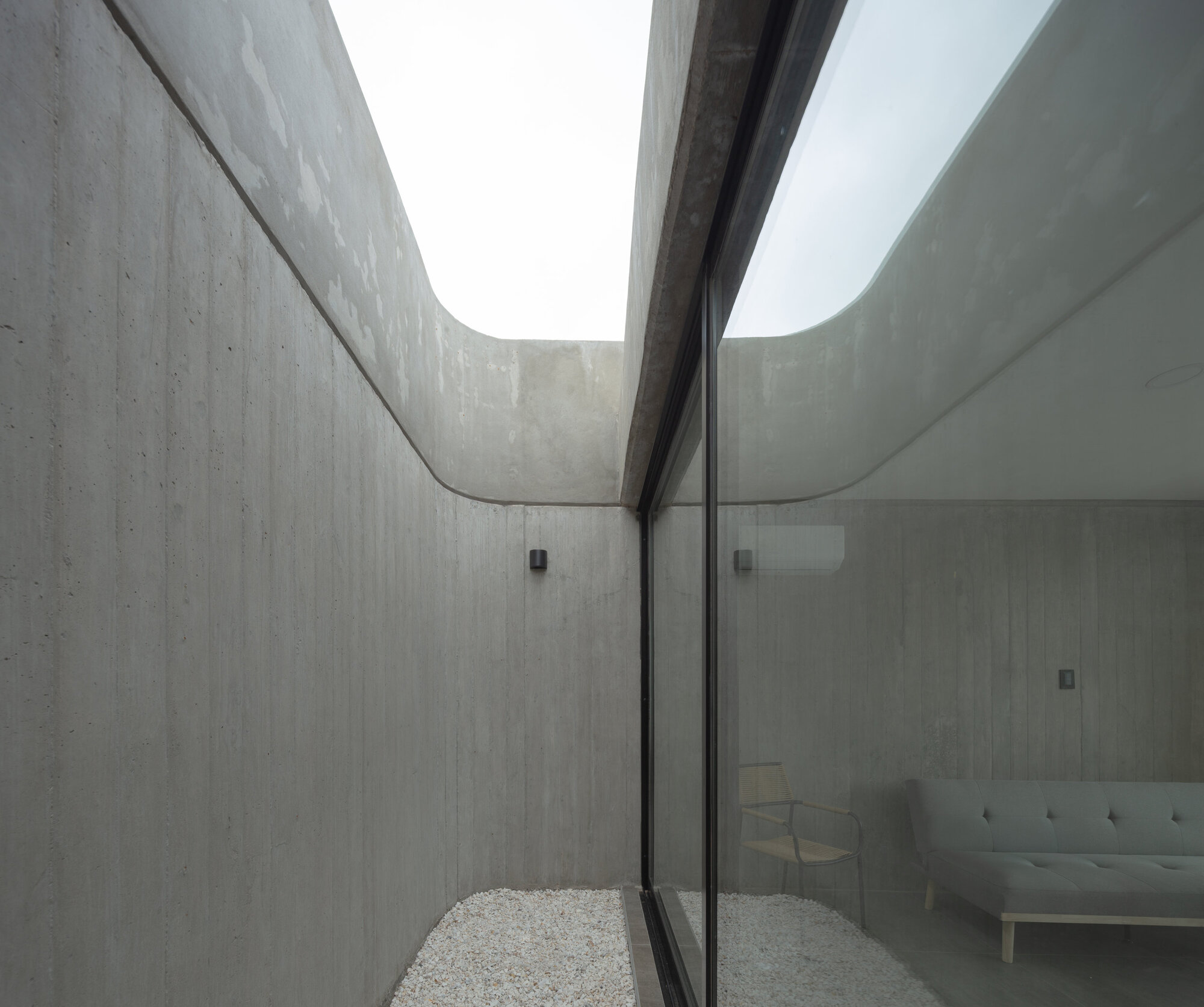 Narrow gravel courtyard between curved concrete walls with a clerestory opening above