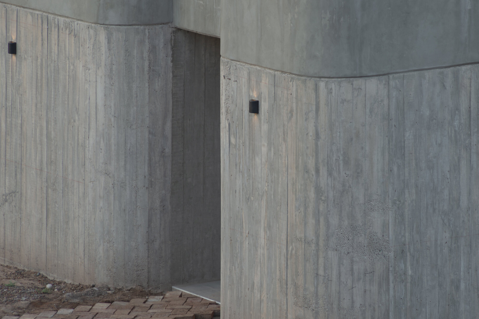 Close-up of curved board-formed concrete walls meeting at angular corners in flat light