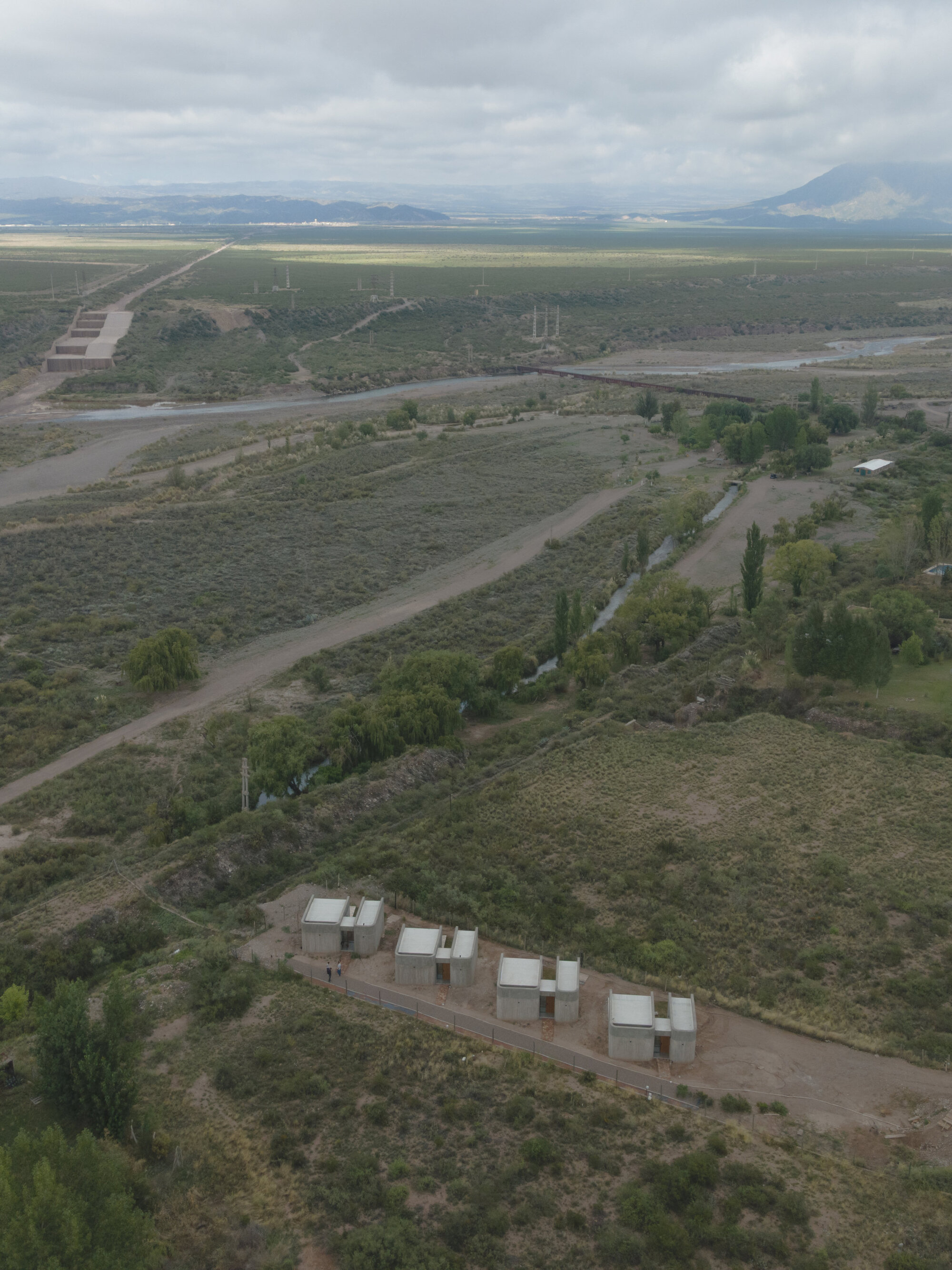 Oblique aerial view of four paired white housing units along a road with distant mountains and cloudy sky