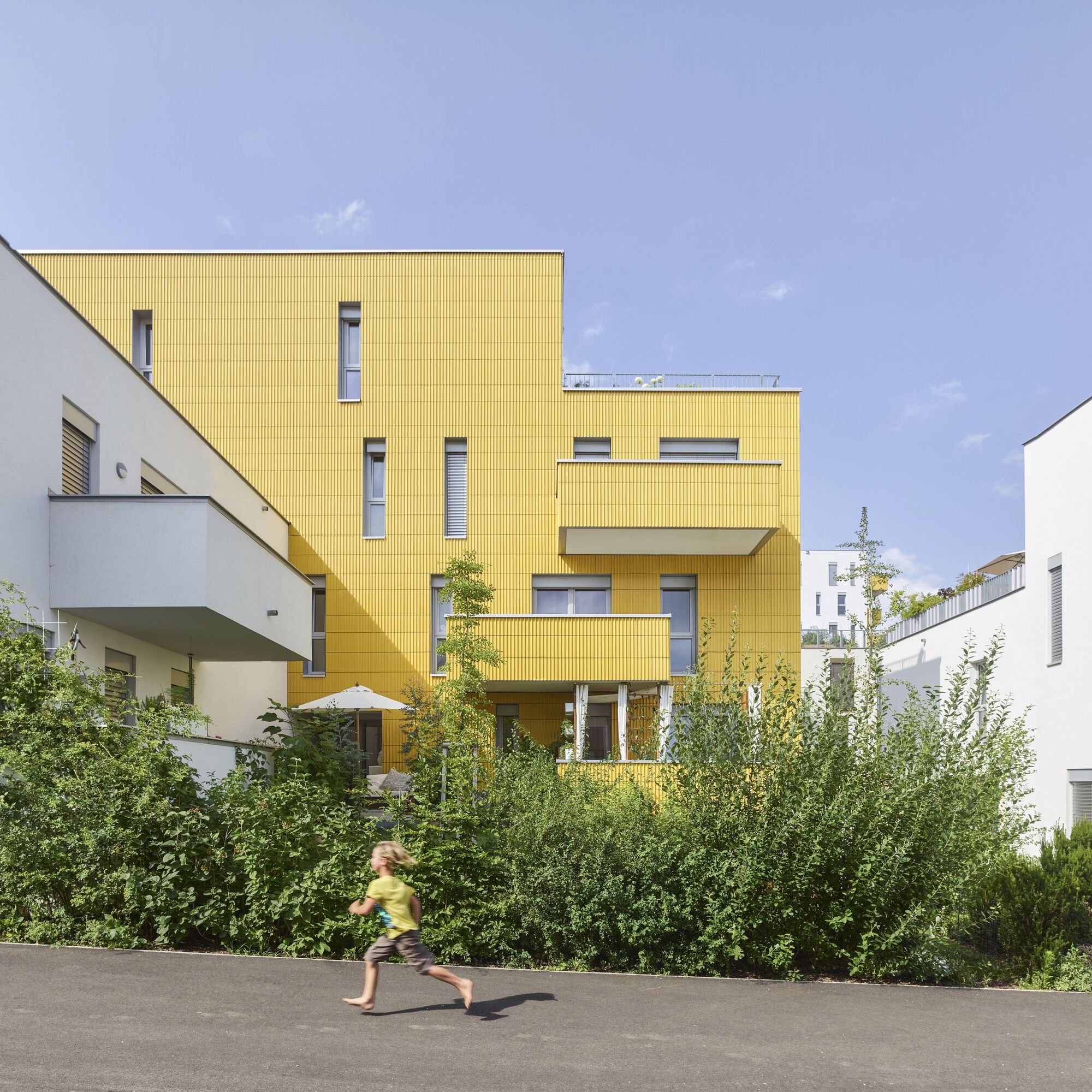 Stepped volume clad in yellow corrugated panels with a child running along the asphalt path