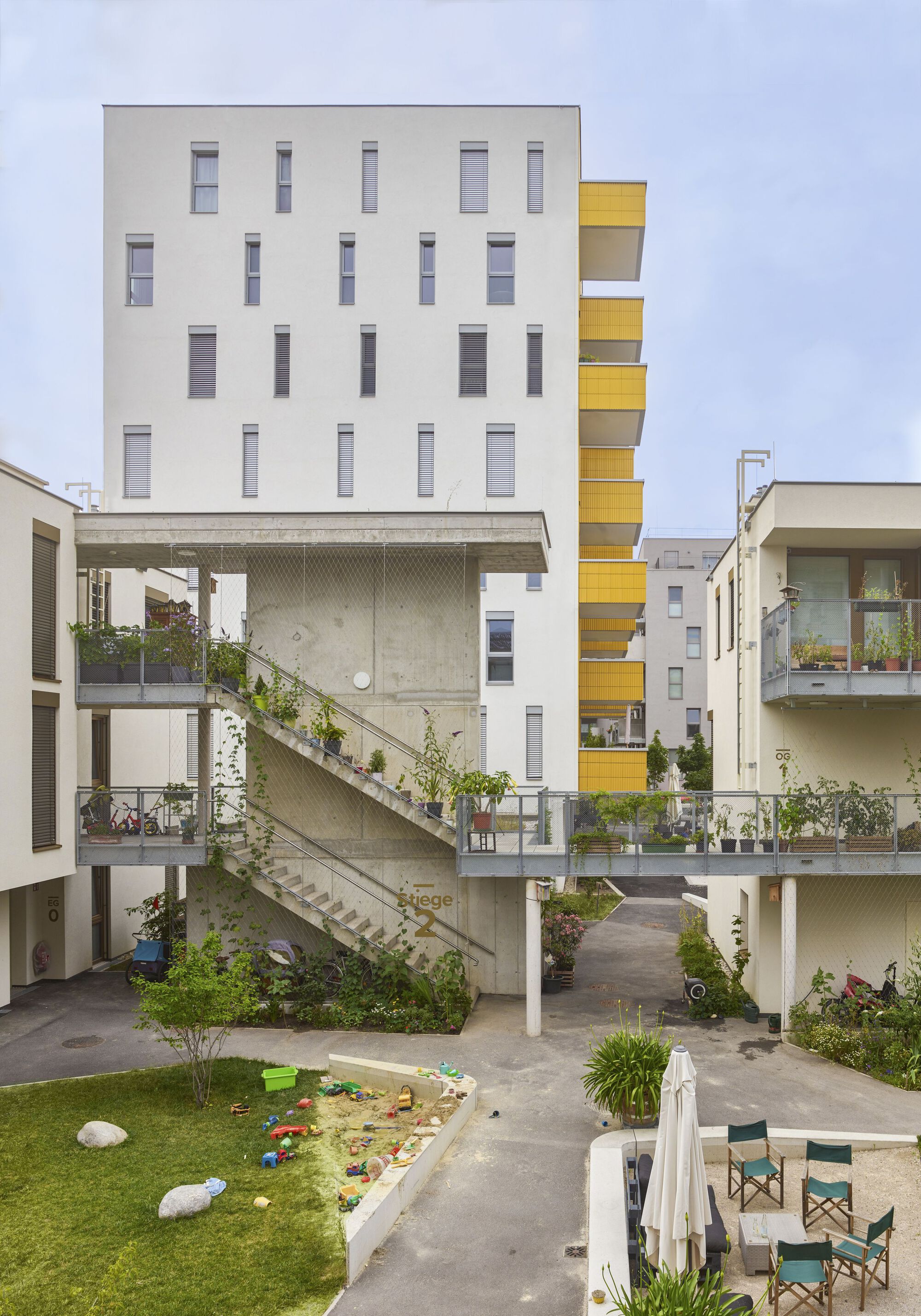 Diagonal concrete staircase connecting courtyard levels with planted balconies and play area below