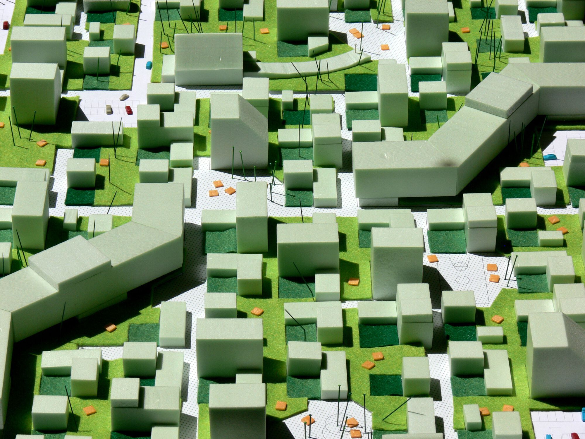 Physical model showing massing arrangement with green foam volumes, white paved surfaces, and small orange accent pieces