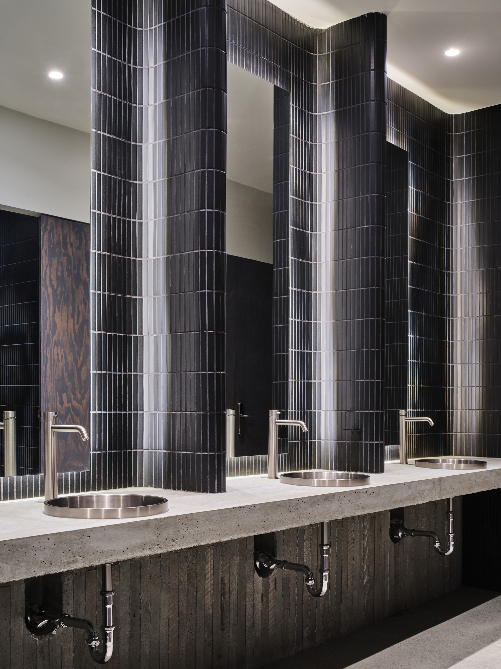 Restroom vanity with terrazzo counter, round metal sinks and vertically ribbed black tile wall panels