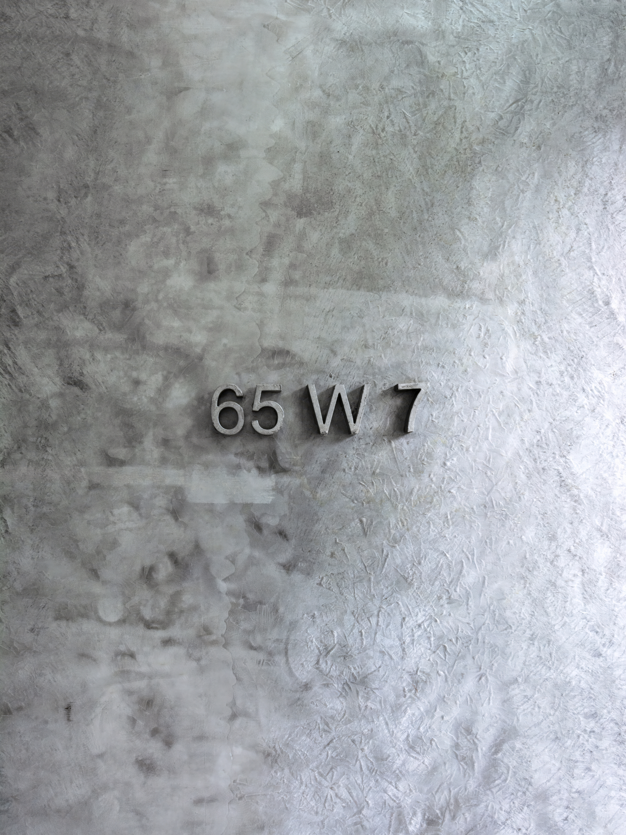 Metallic address numbers mounted on a textured concrete wall with weathered patina