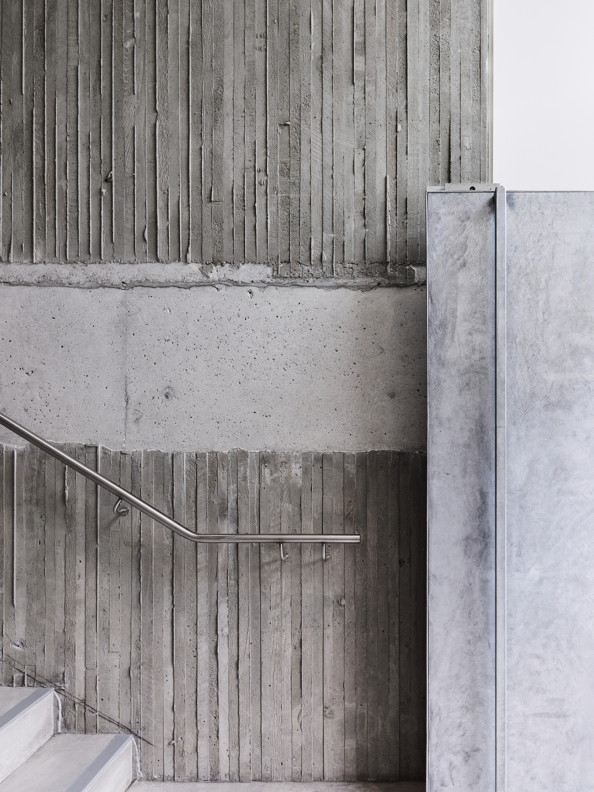 Board-formed concrete wall with stainless steel handrail alongside white painted masonry wall