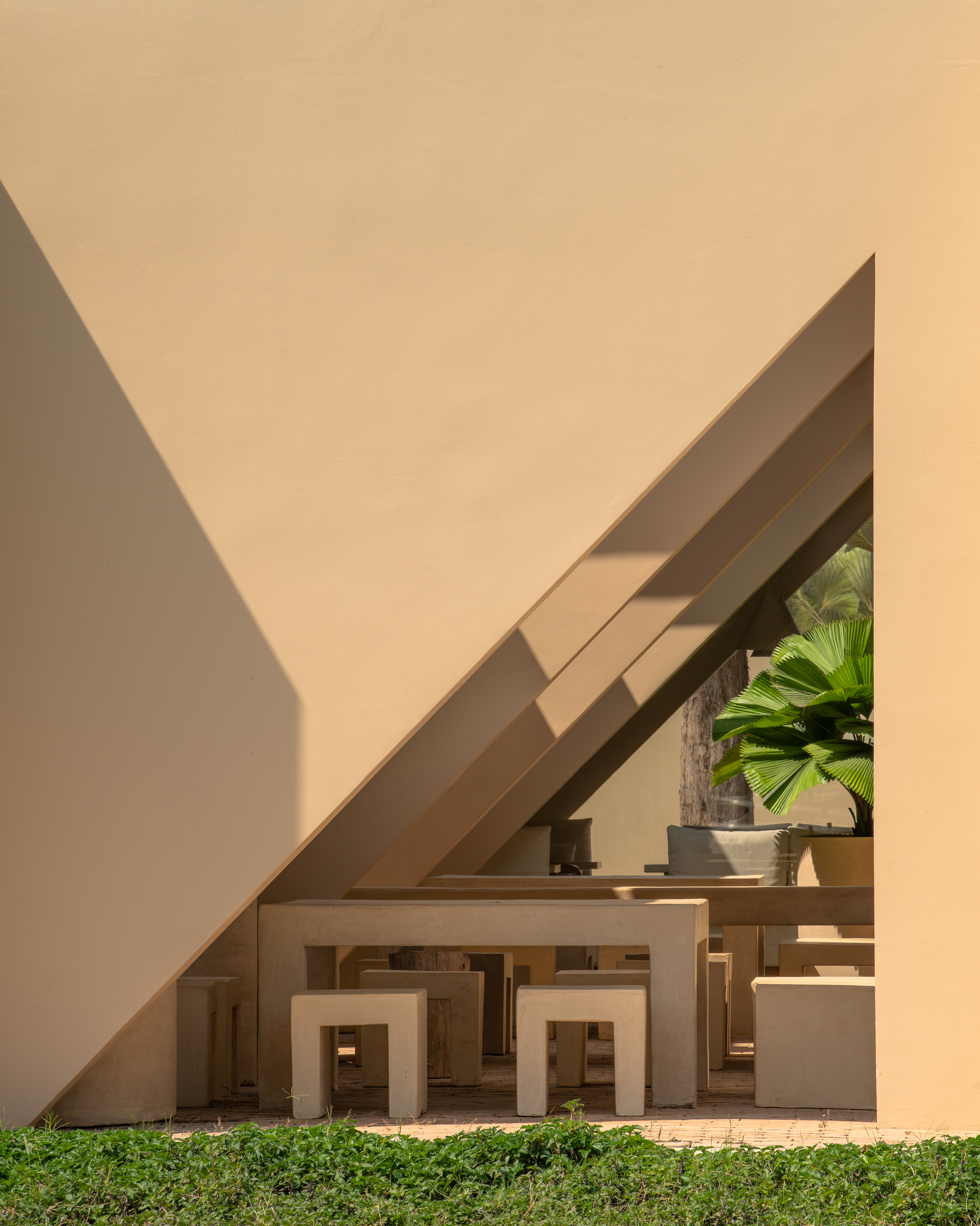Courtyard view of stacked beige stucco frames beneath an angled roof with palm trees visible beyond