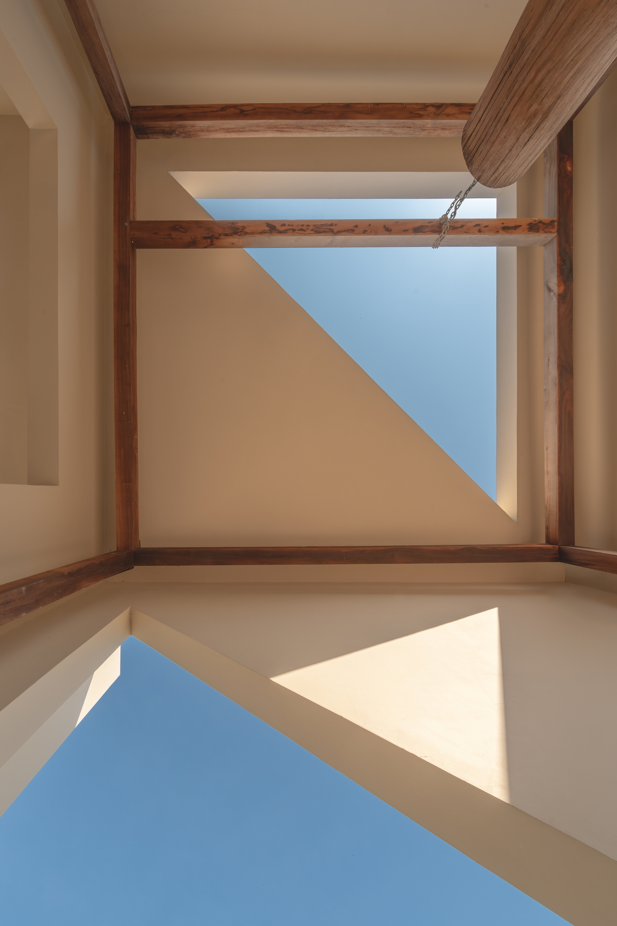 Upward view of skylight framed by timber beams showing blue sky and diagonal shadows