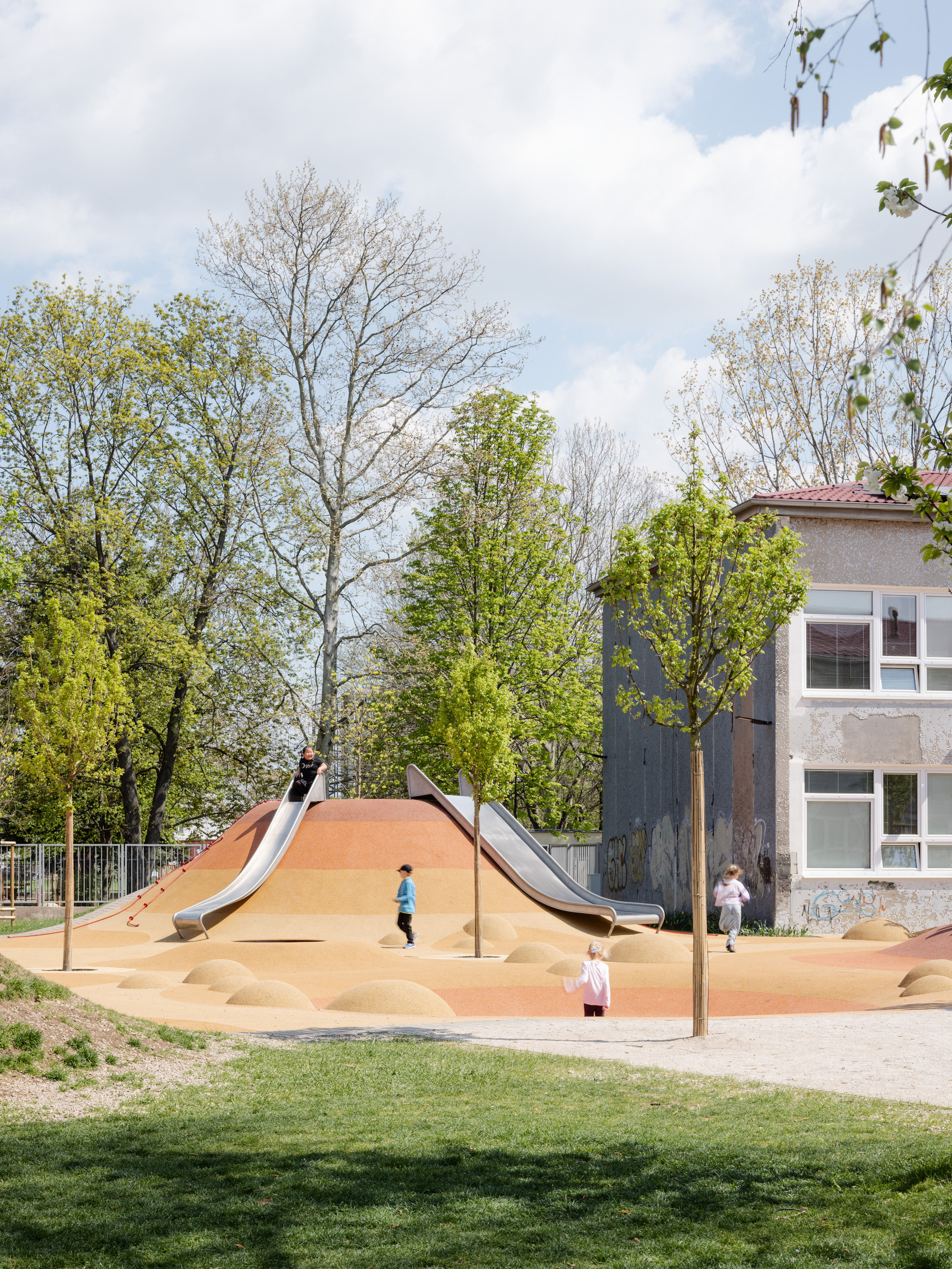 Play area with twin slides on a sand dune and children moving between young trees