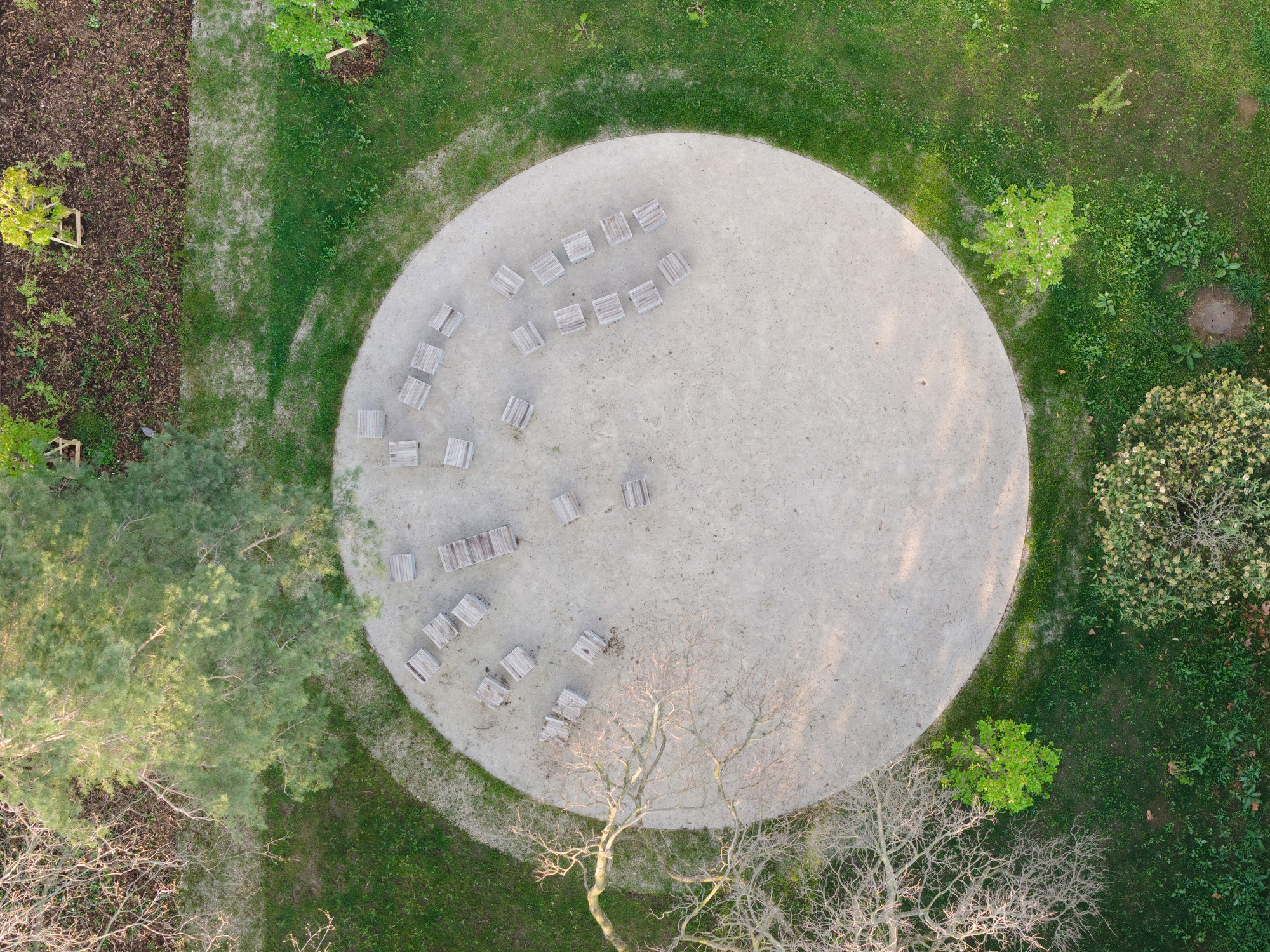 Drone view of a circular concrete plaza with perimeter seating surrounded by grass and trees