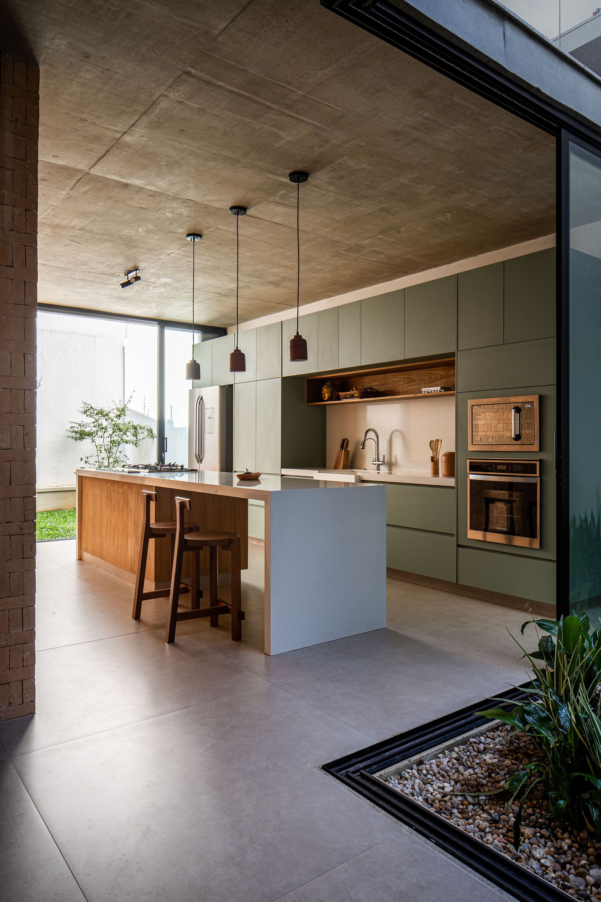 Kitchen with sage green cabinetry, timber island and pendant lights under exposed concrete ceiling