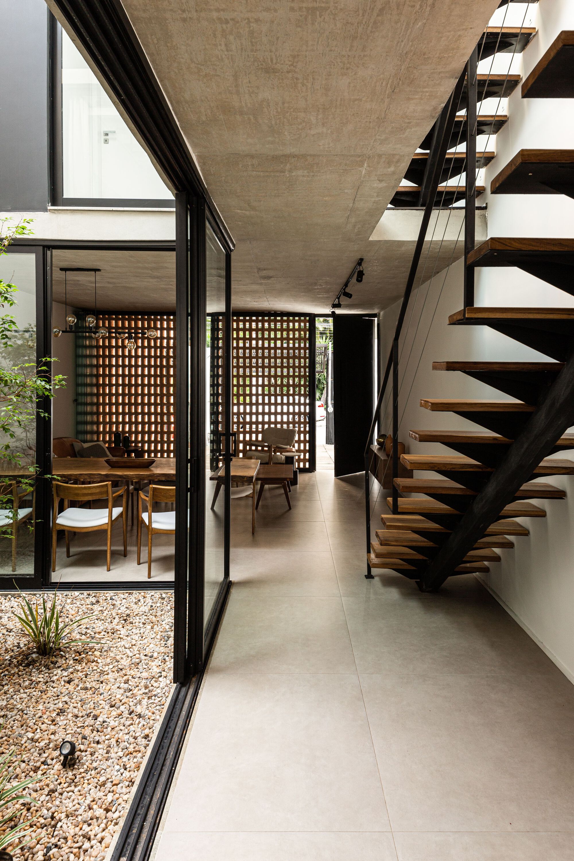 Open-tread staircase with steel stringers and glass railing beside glazed courtyard wall