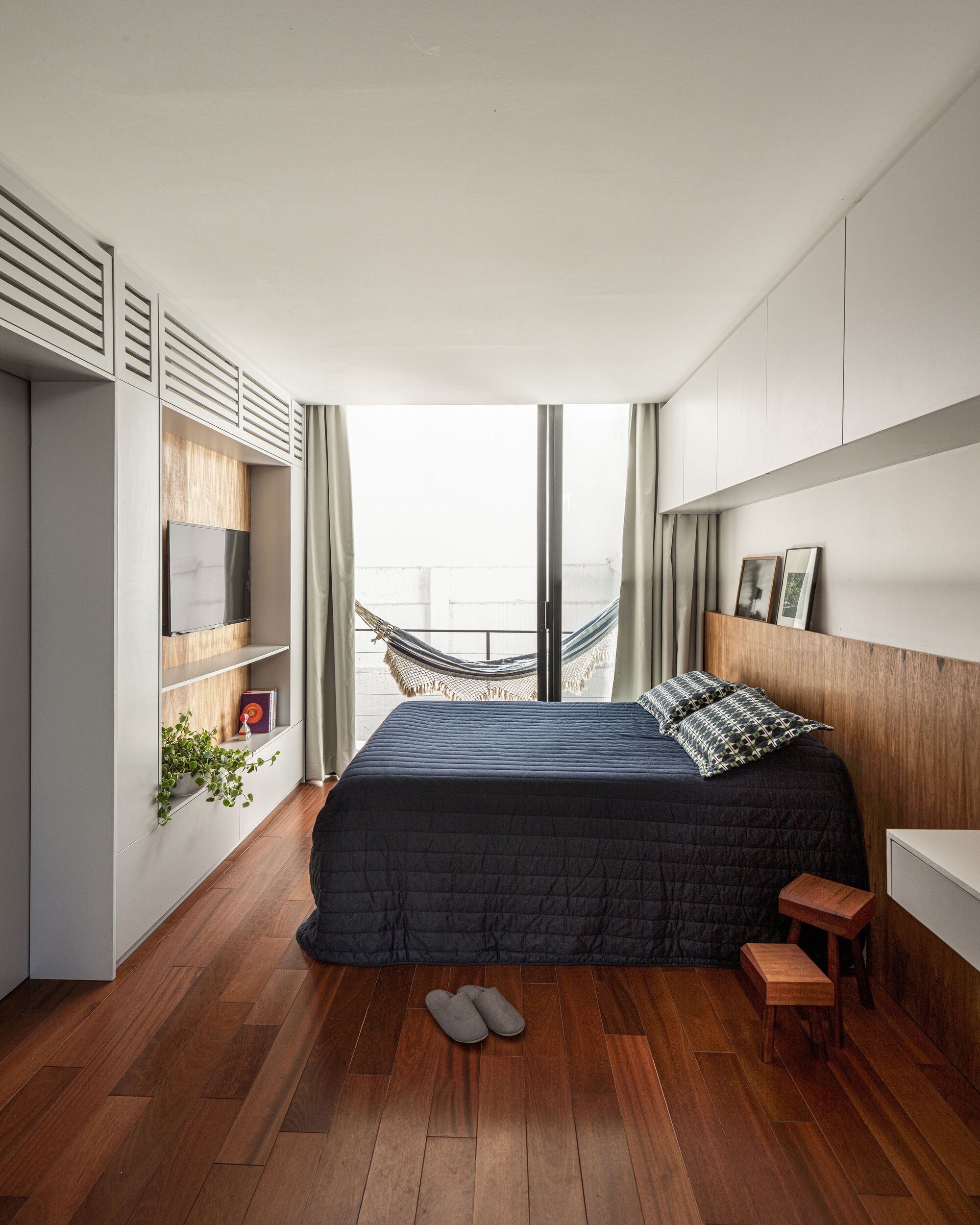 Bedroom with hammock suspended in balcony doorway and white storage cabinetry with timber accents