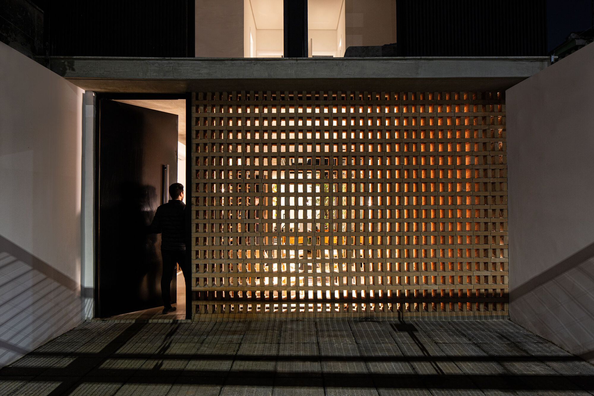 Backlit perforated brick screen with figure in doorway at dusk