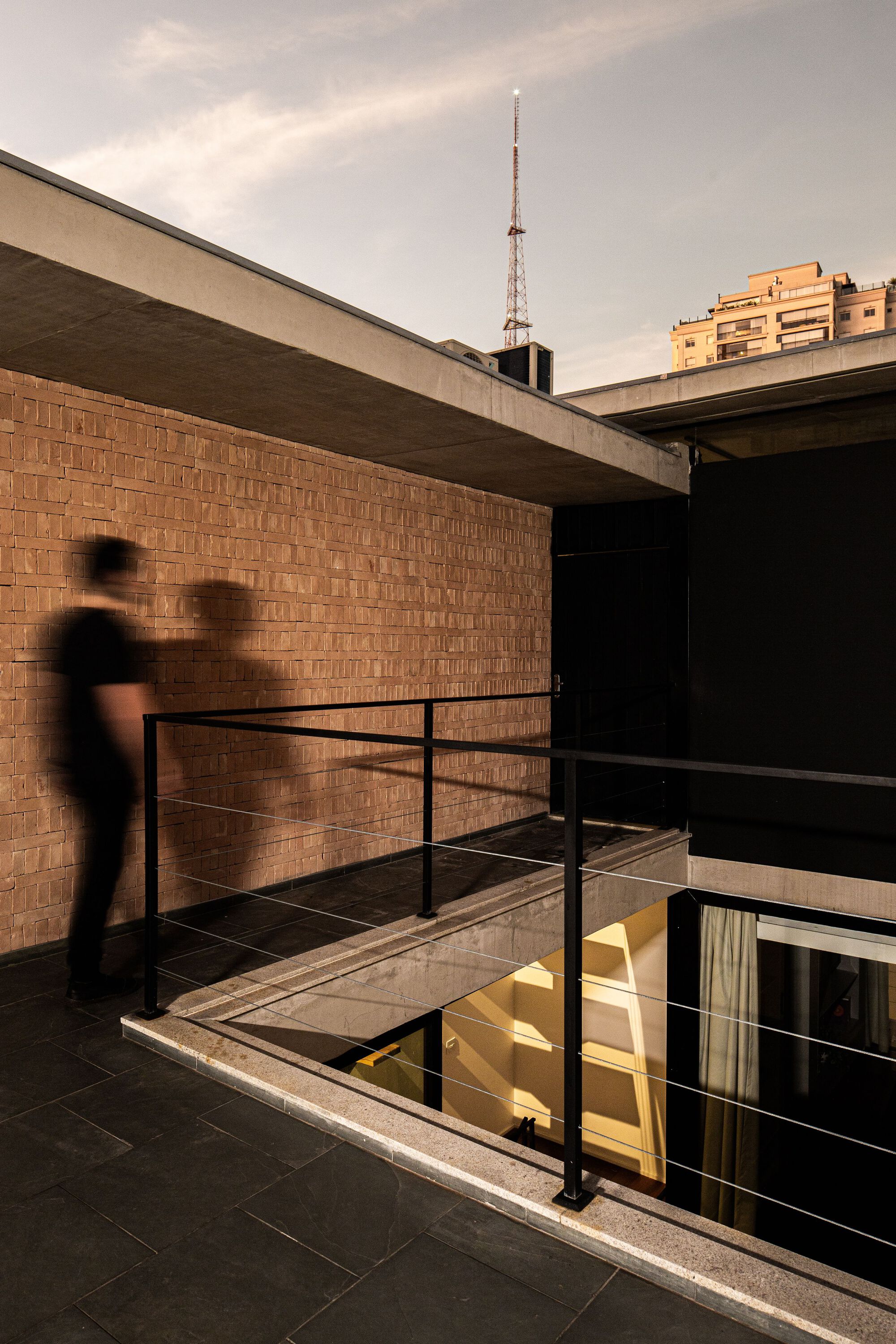 Rooftop terrace with black metal railing and glazed skylight opening at golden hour