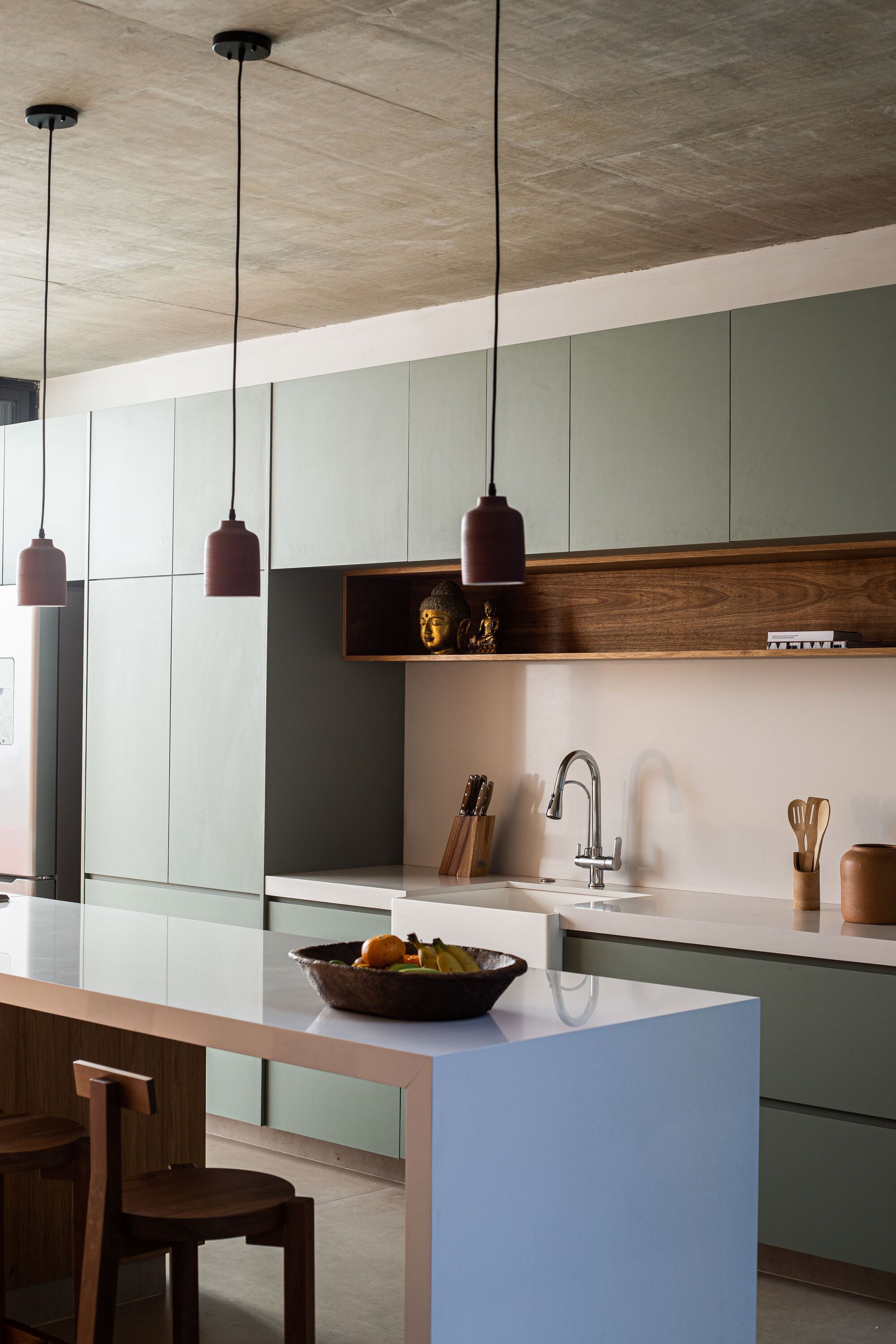 Kitchen island with white stone top beneath three cylindrical pendant lights and plywood ceiling