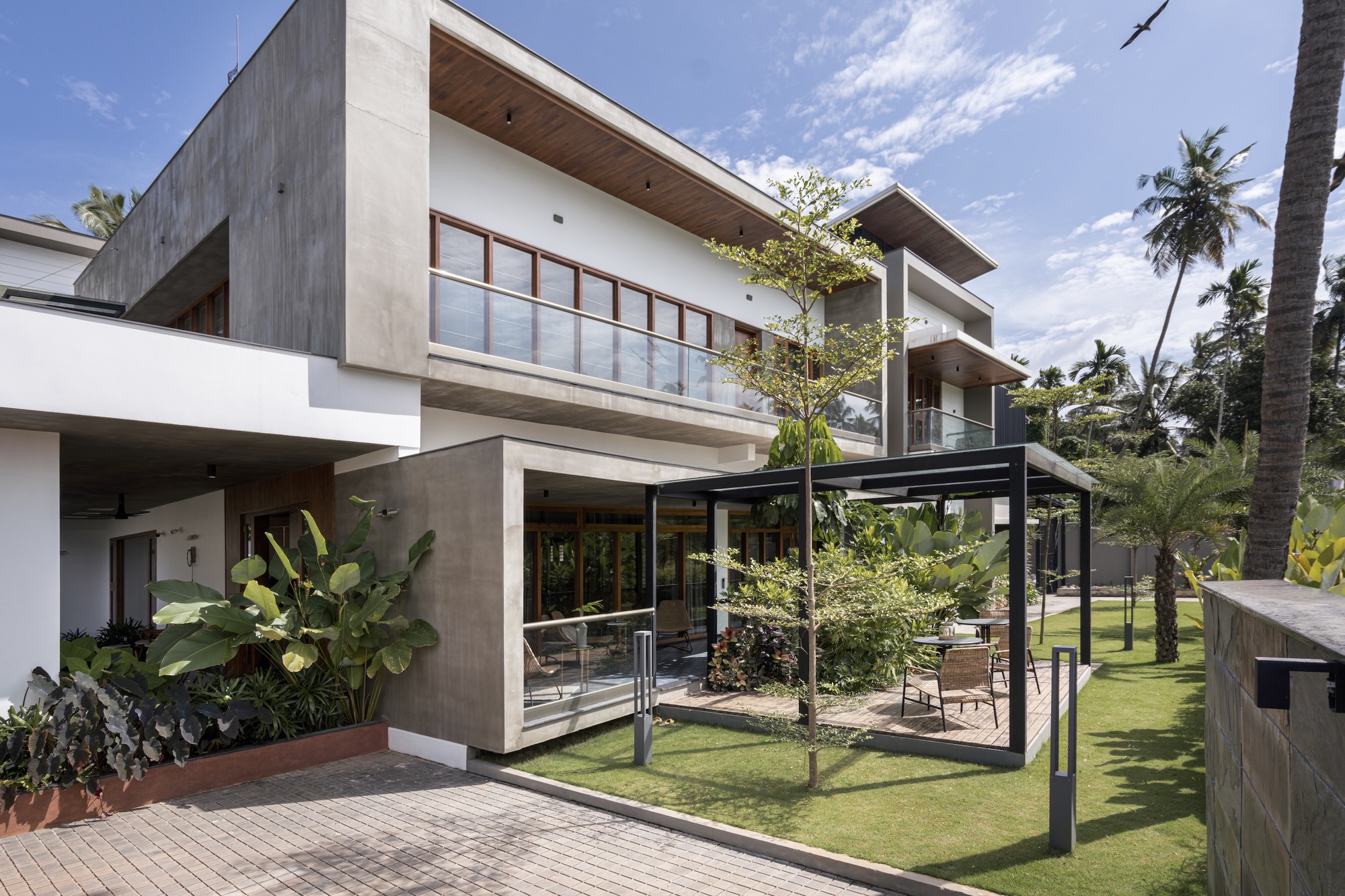 Garden view of the stacked concrete and white volumes with steel-framed pergola surrounded by palm trees