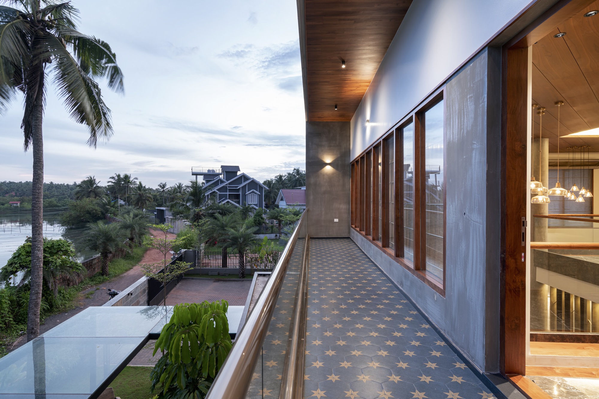 Exterior corridor at dusk with patterned tile floor, timber ceiling soffit, and timber screens beside palm trees