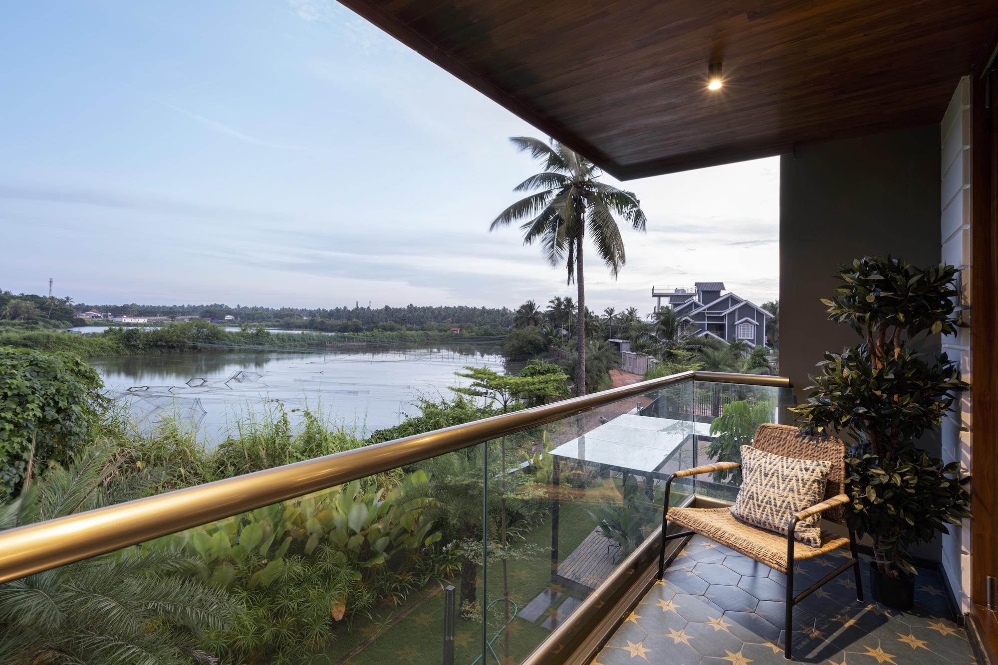 Covered balcony with timber soffit and glass railing overlooking a palm-lined river at dusk