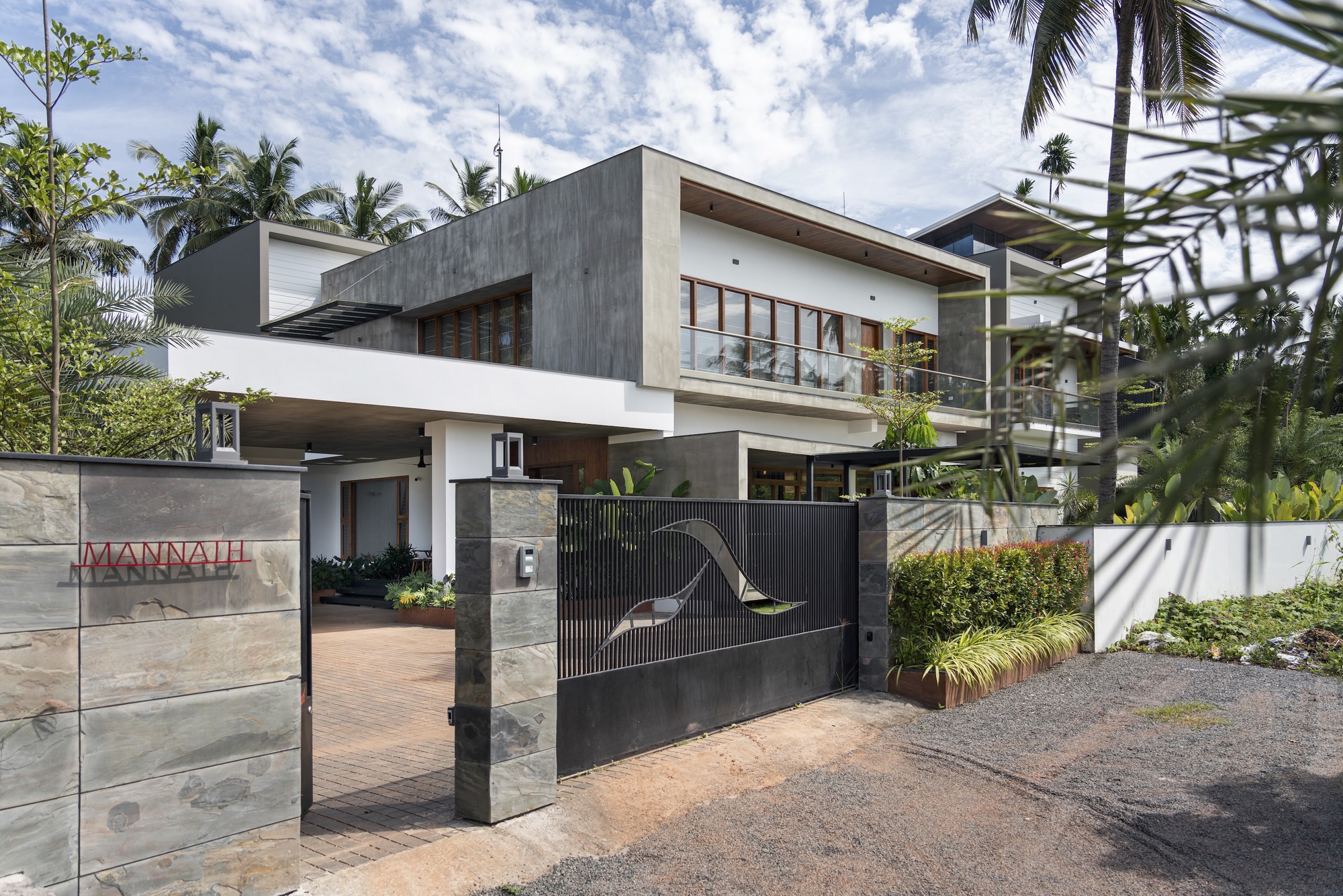 Street view of the two-story facade with concrete panels and timber screens amid palms