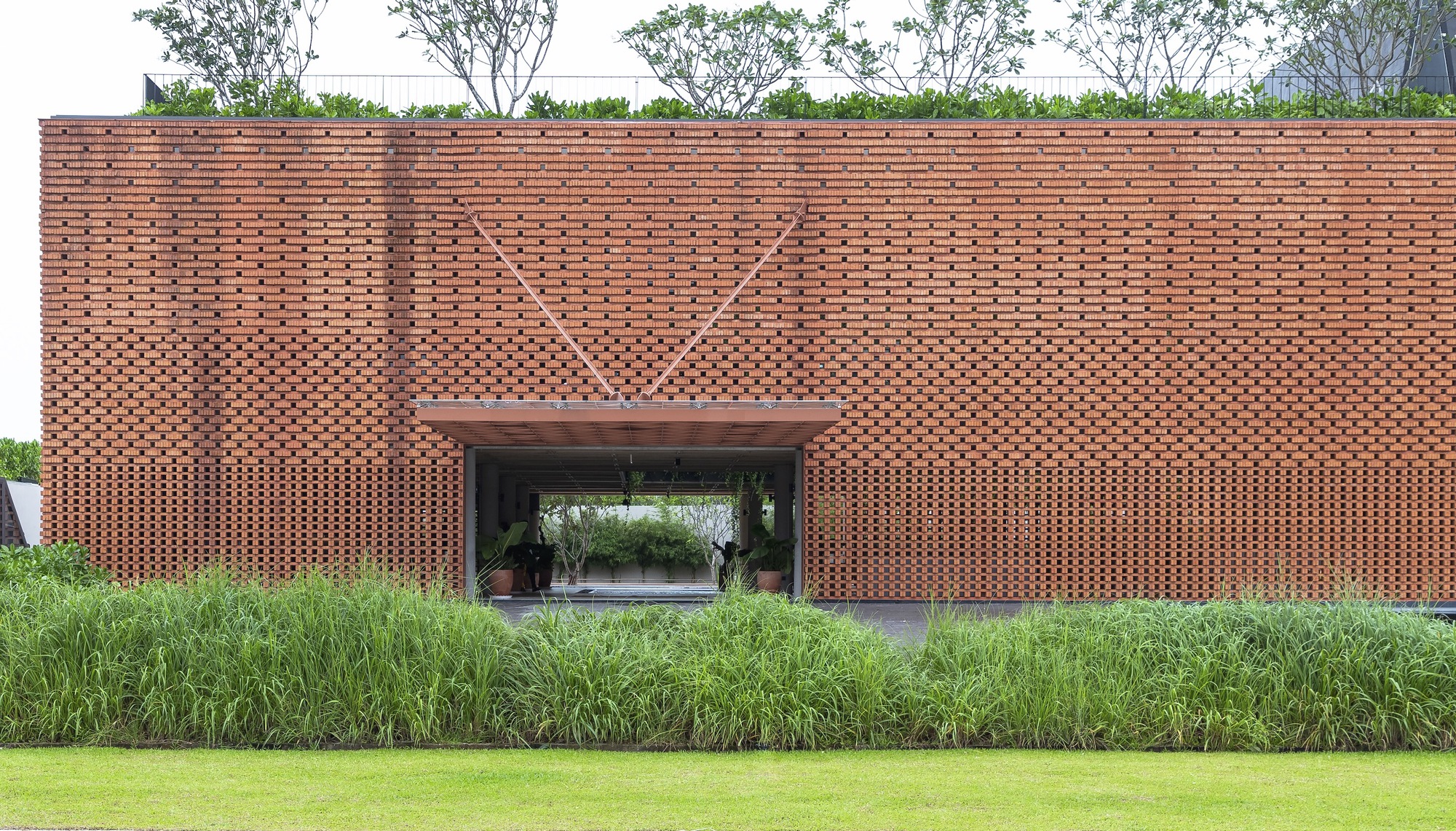 Perforated brick facade with chevron pattern above a central passage, fronted by planted beds and lawn