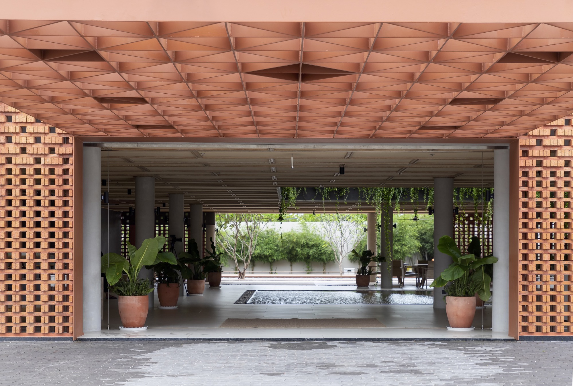 Covered entry passage with geometric timber ceiling and open brick screens flanking potted plants