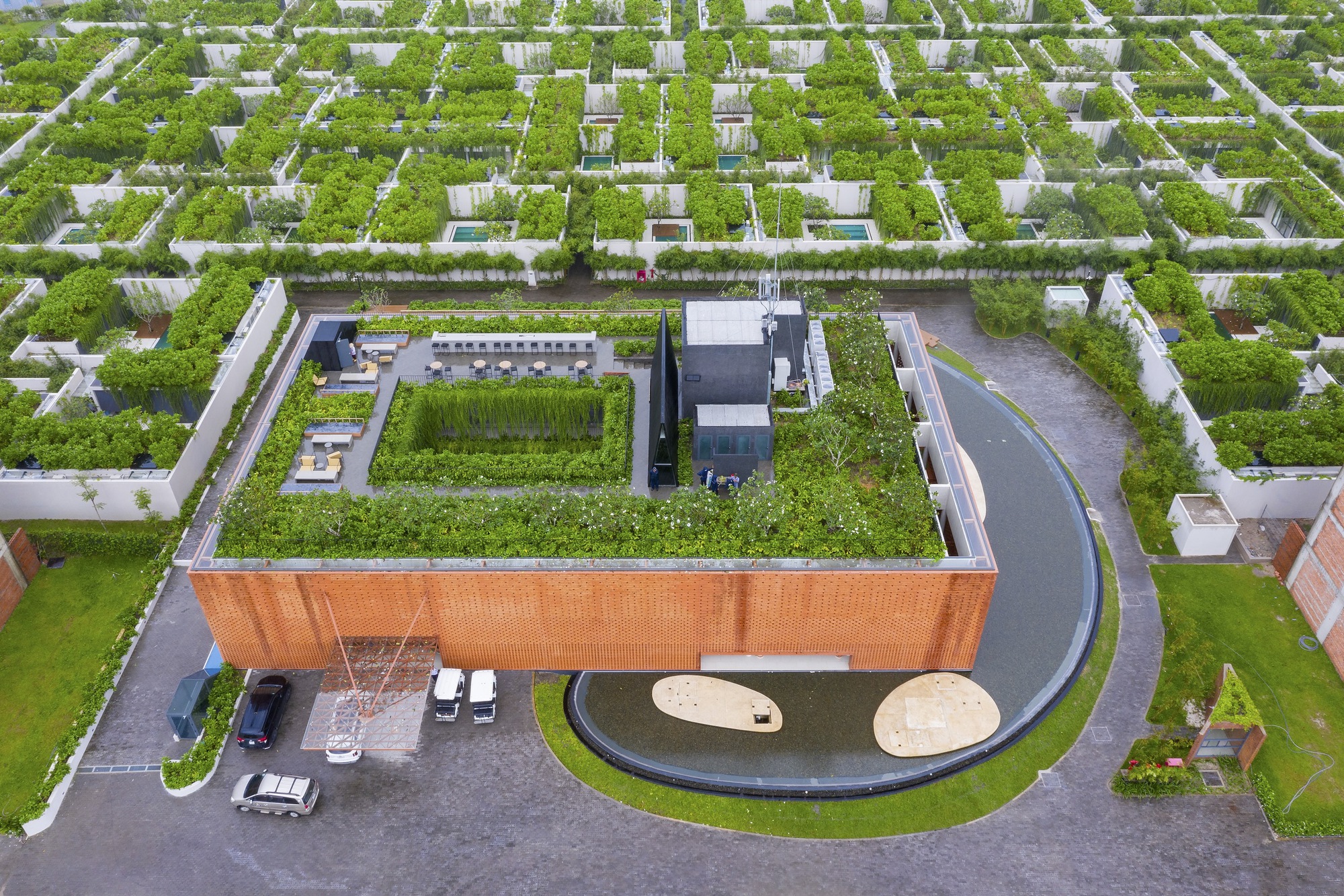 Aerial view of the green-roofed brick building within a grid of planted neighborhood plots