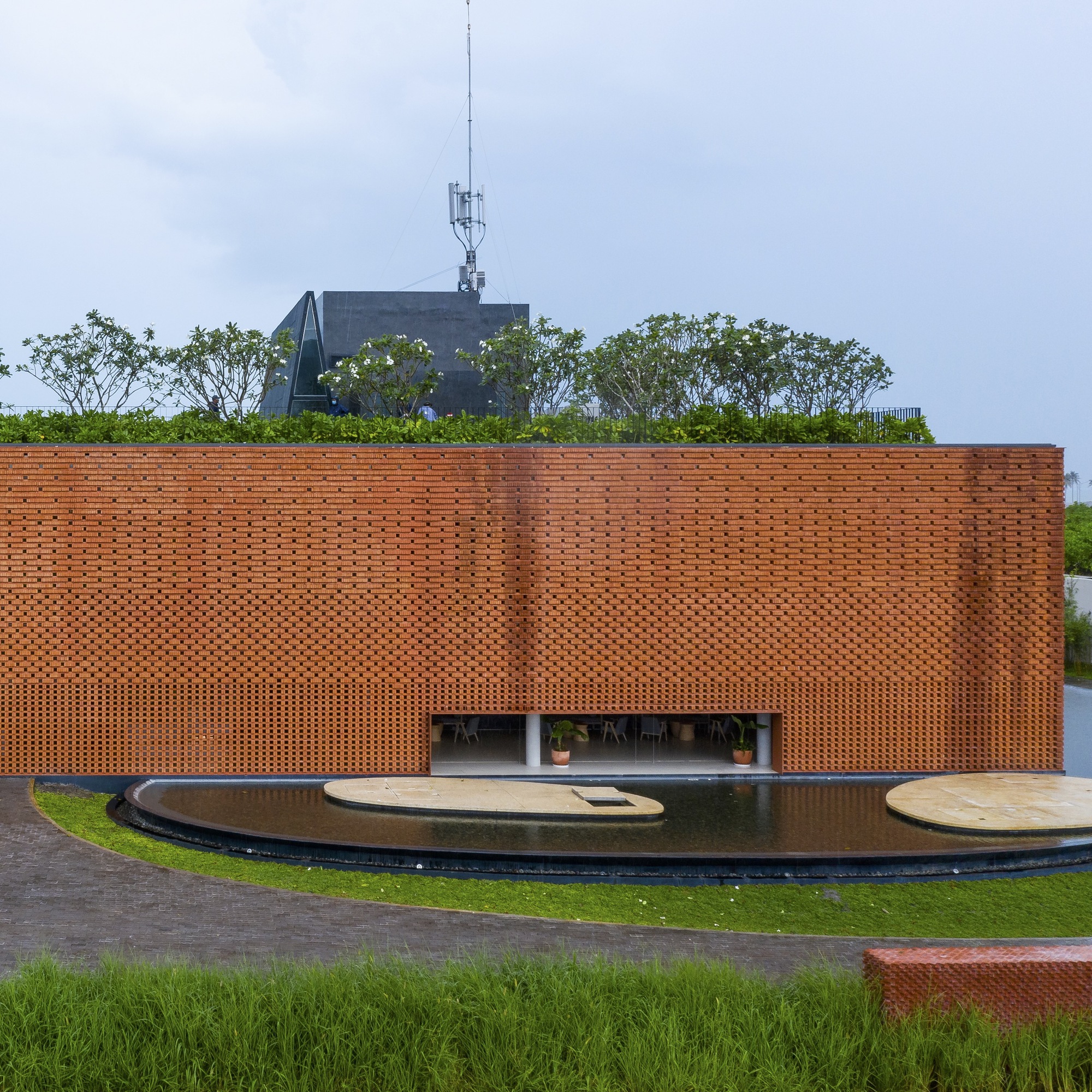 Perforated terracotta brick facade with rooftop garden and curved water feature in front lawn