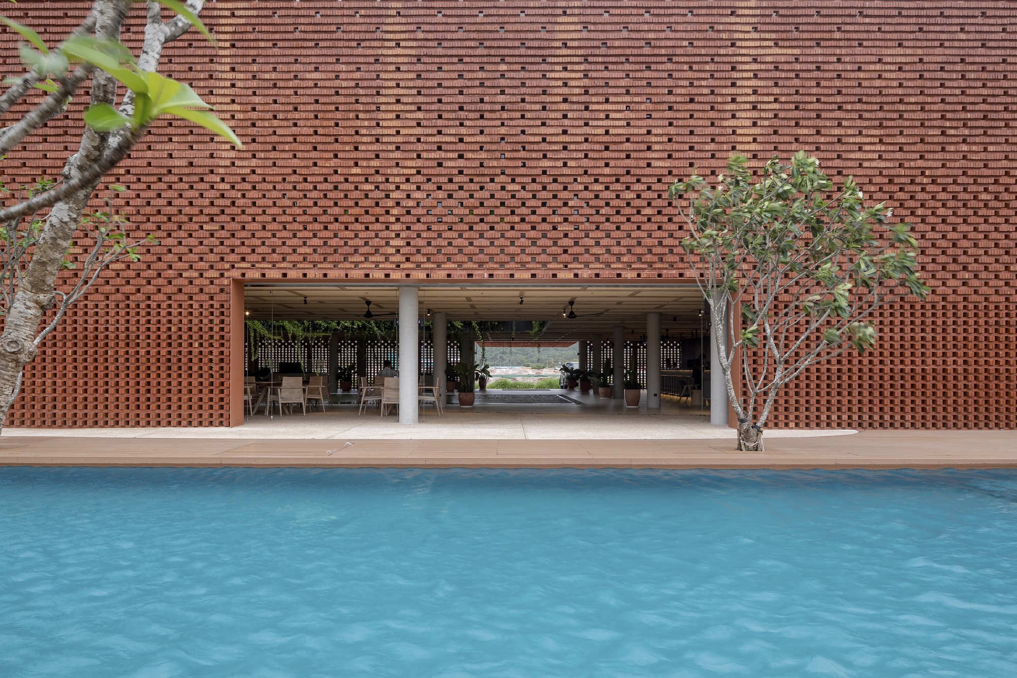 View across swimming pool toward covered pavilion with timber ceiling and potted tree