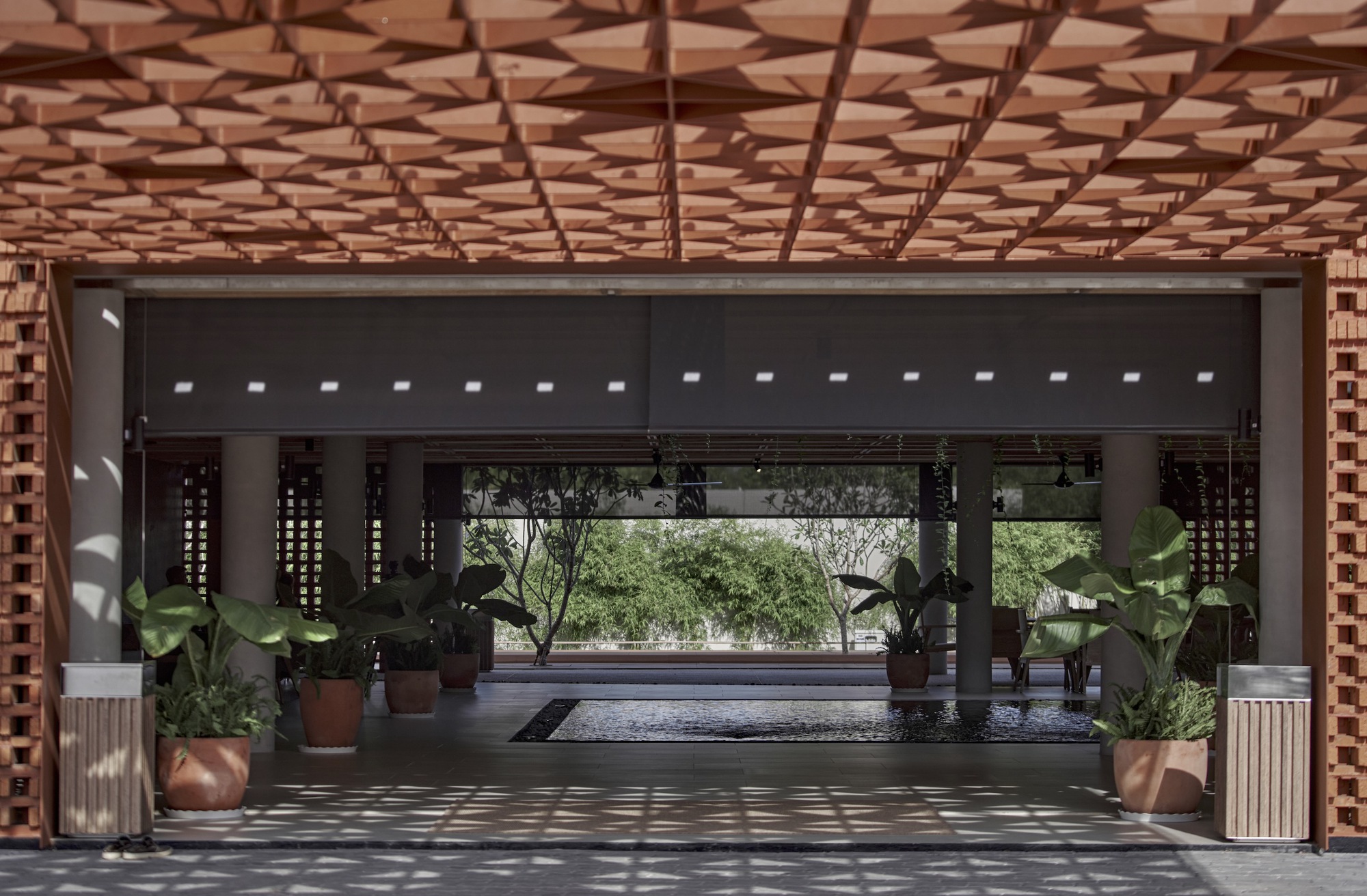 Interior view through covered entry showing perforated timber ceiling and dappled sunlight patterns
