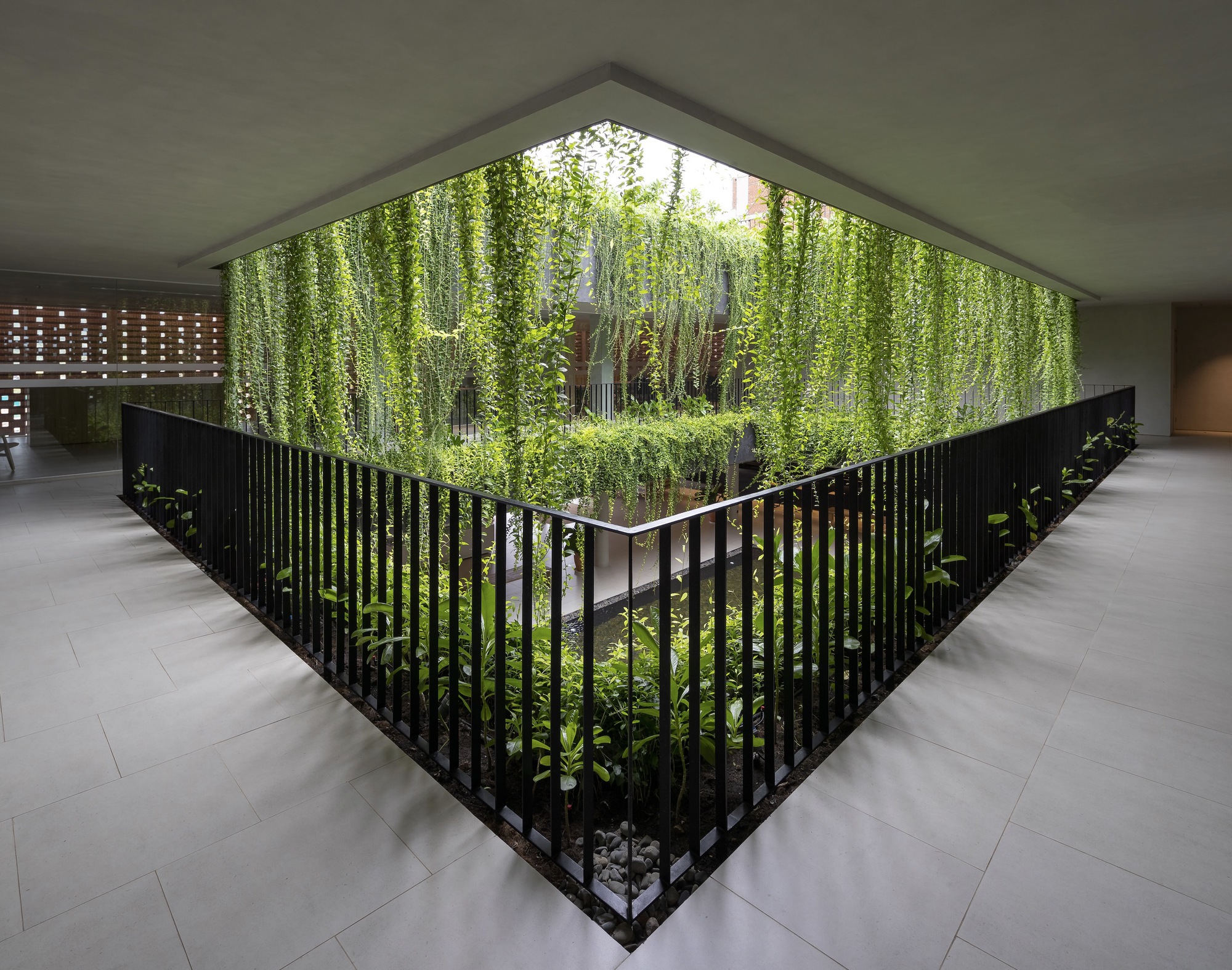 Triangular interior courtyard with black vertical railings enclosing a planted garden and cascading greenery above