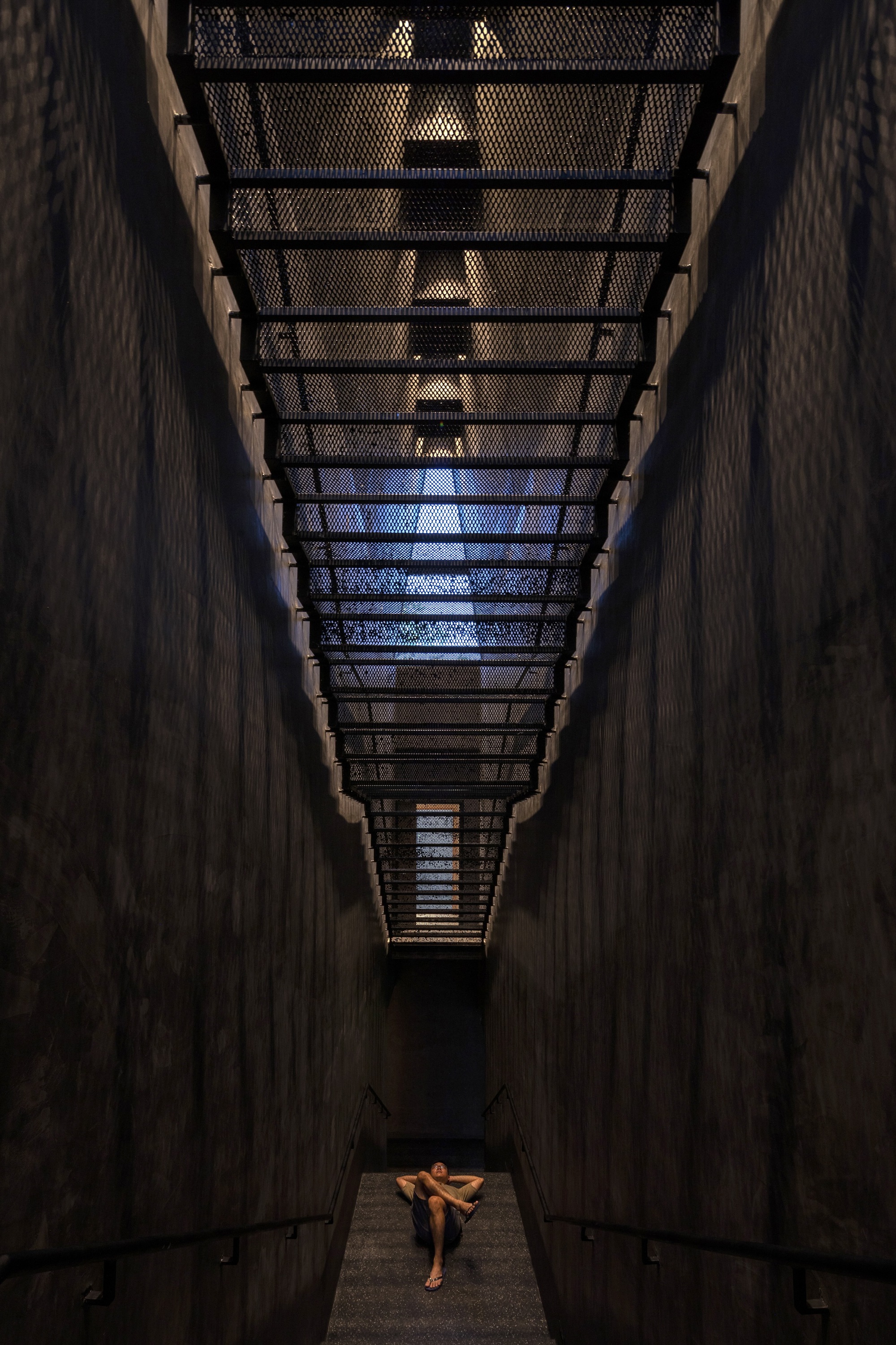 Upward view of narrow skylight with perforated metal screen and timber walls framing a figure below