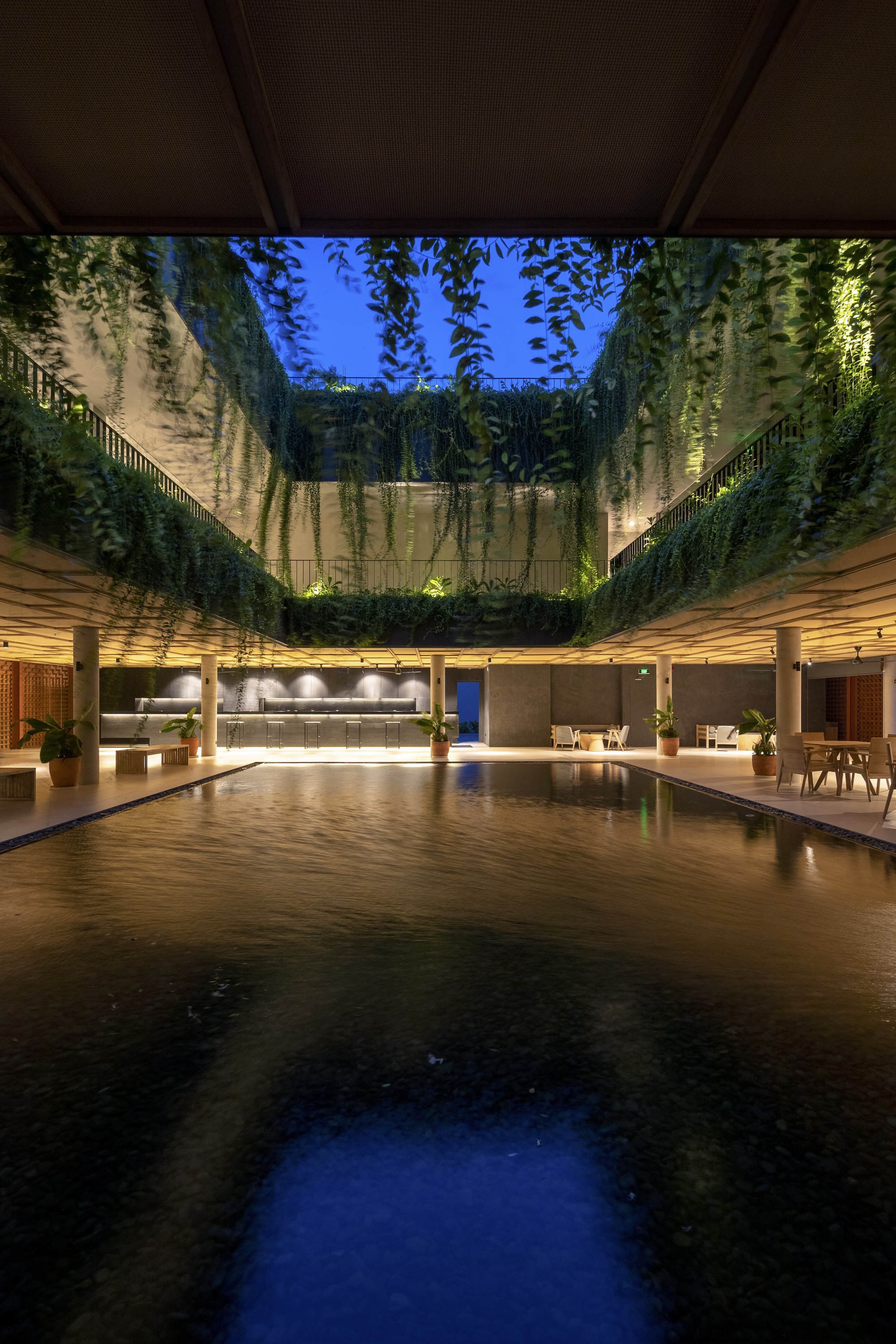 Open courtyard pool with cascading green walls rising toward a blue twilight sky